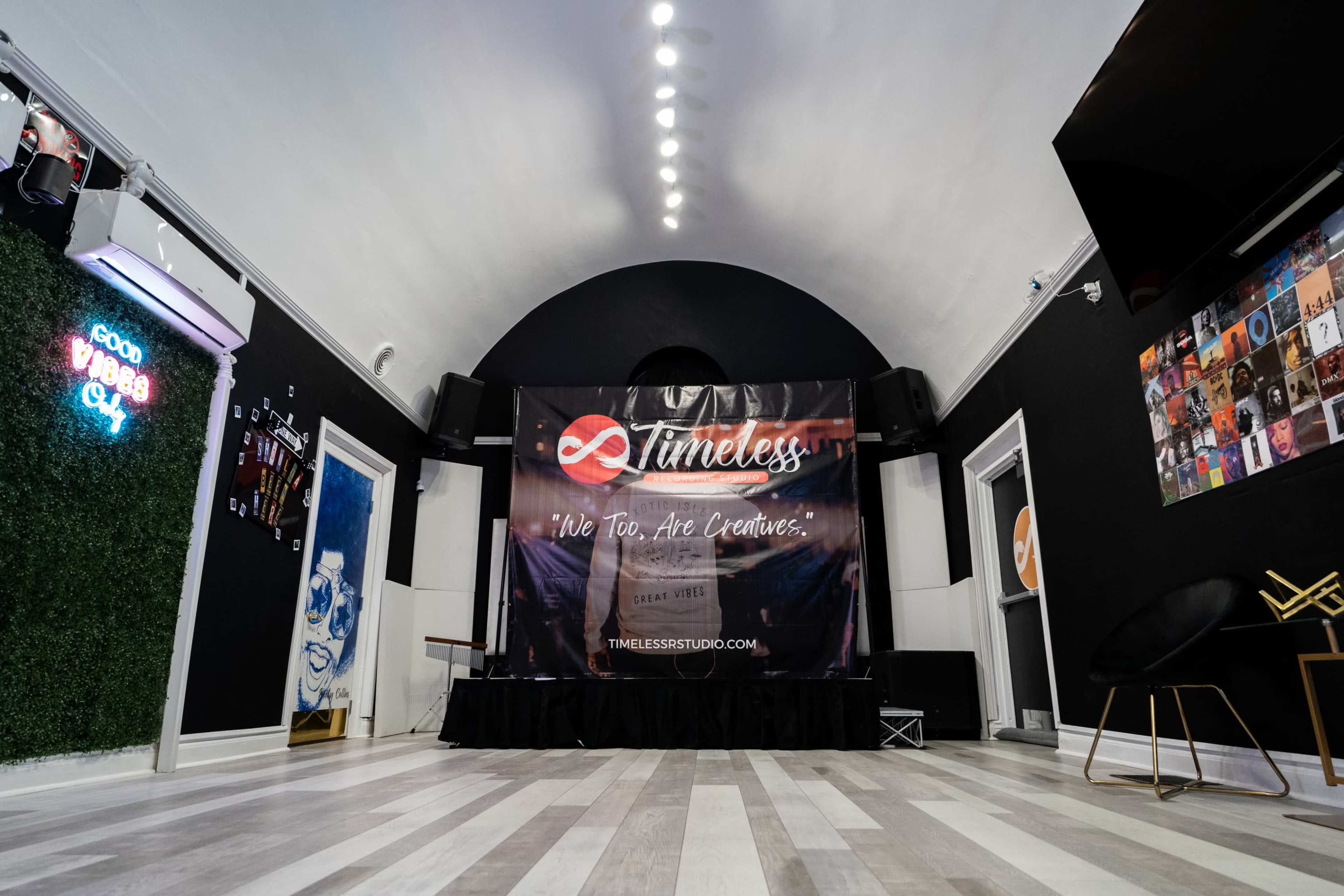 The image shows a modern studio space featuring a mounted banner with the text "Timeless" and a performance area with light wood flooring and decorative elements on the walls.