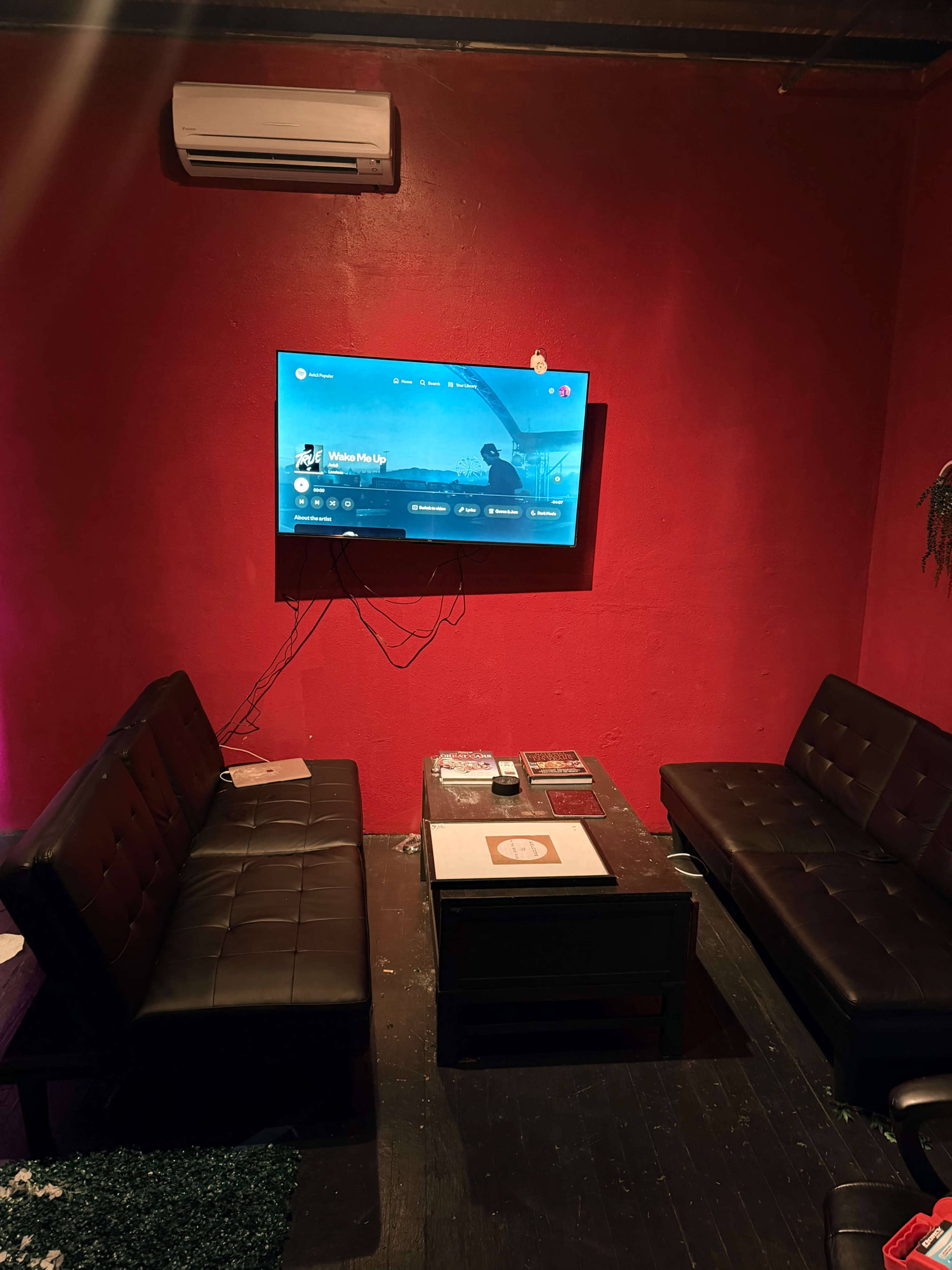 The image shows a room with a red wall, two black couches facing each other, a dark coffee table in the center, and a television mounted on the wall displaying a streaming interface.