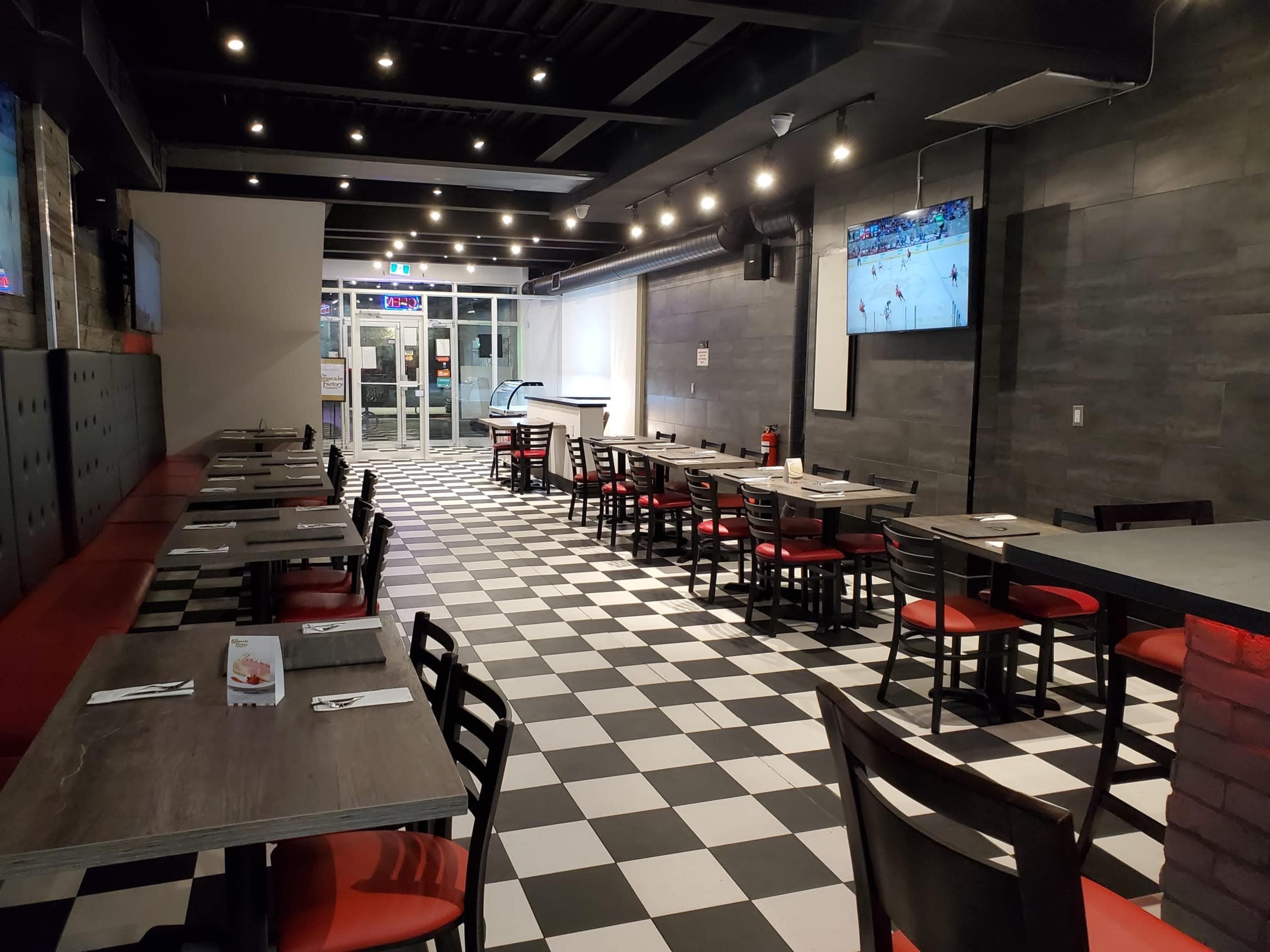 A modern restaurant interior with checkered flooring, red and black seating, and two televisions mounted on the walls.