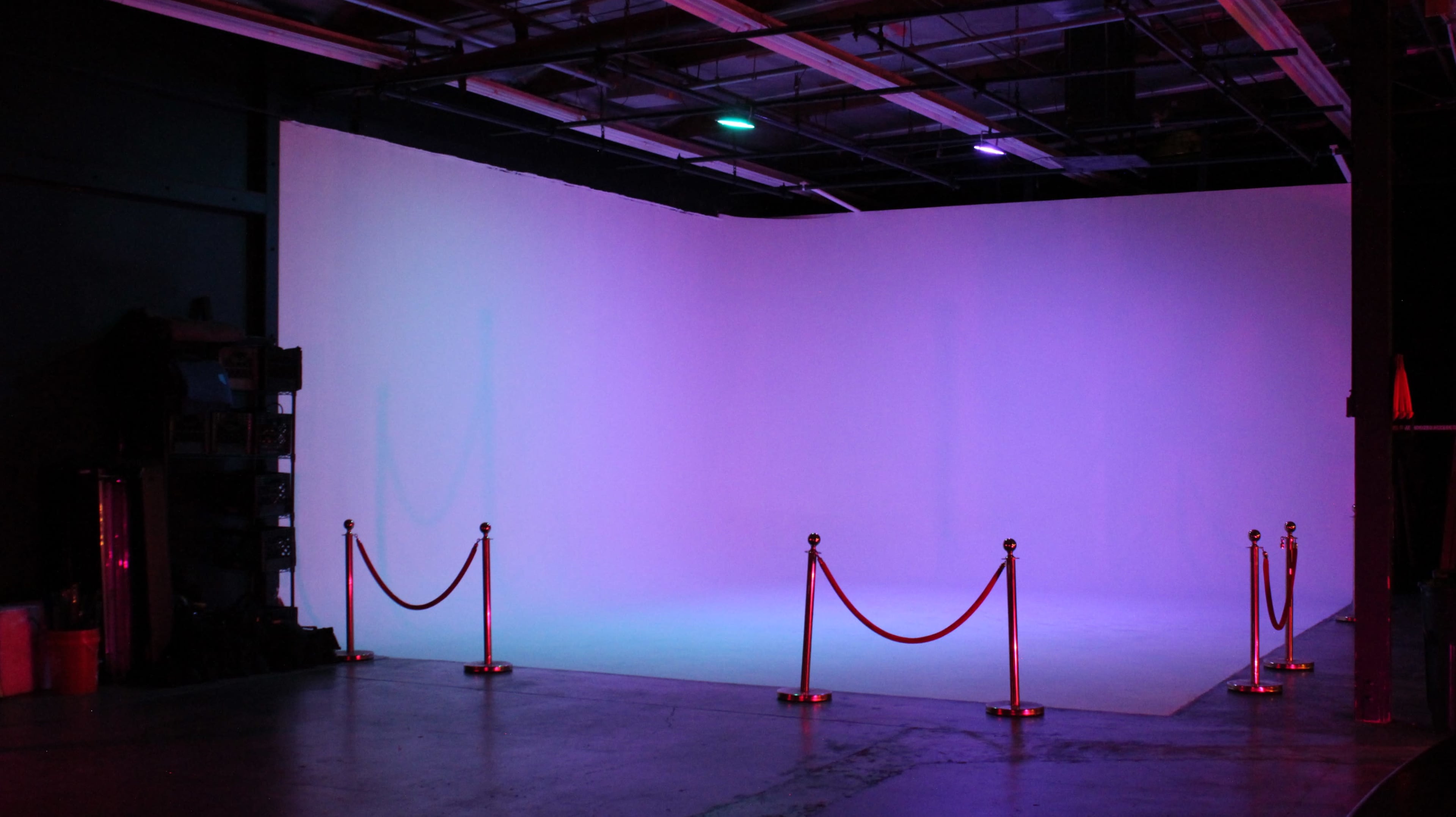 A large empty studio space features a white backdrop with a rope barrier in front.