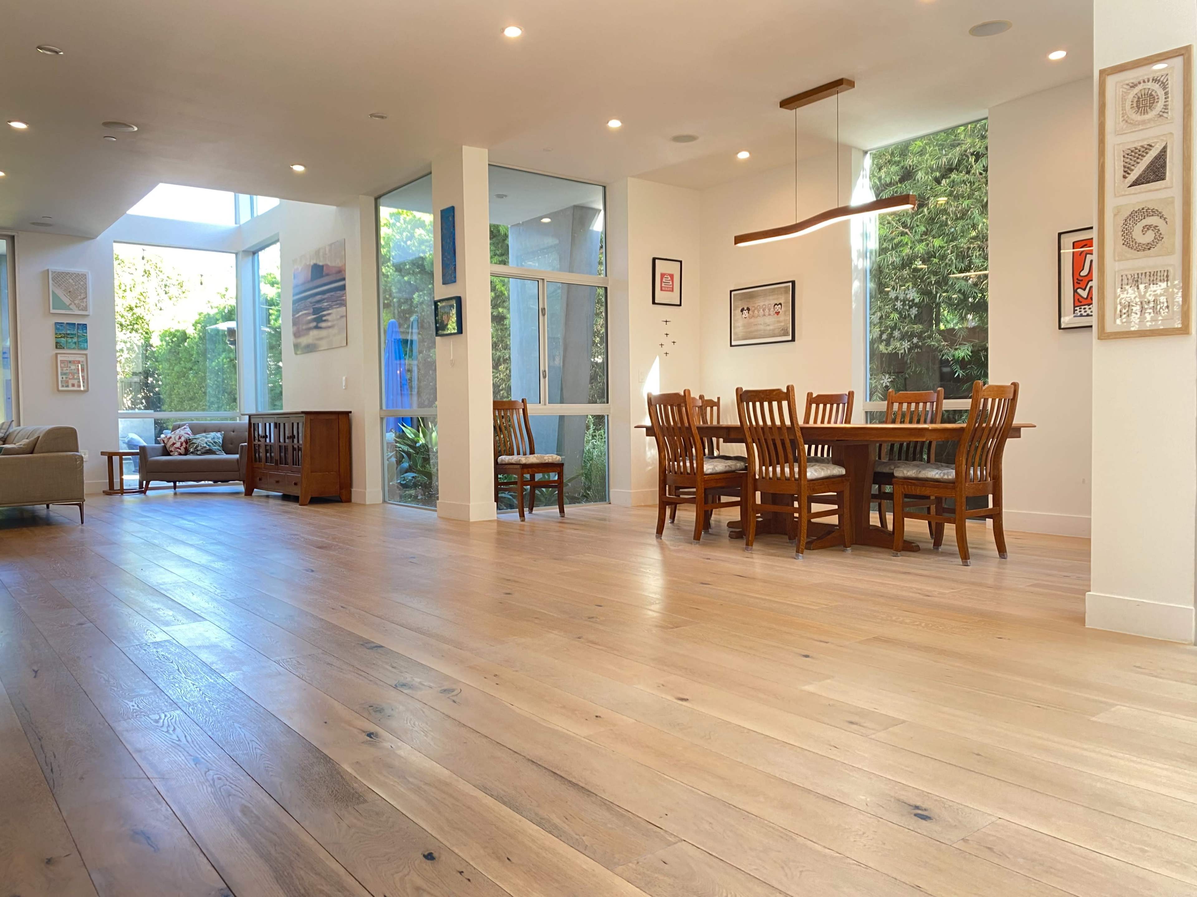 A modern dining area with wooden flooring, a rectangular table surrounded by chairs, and large windows allowing natural light to fill the space.