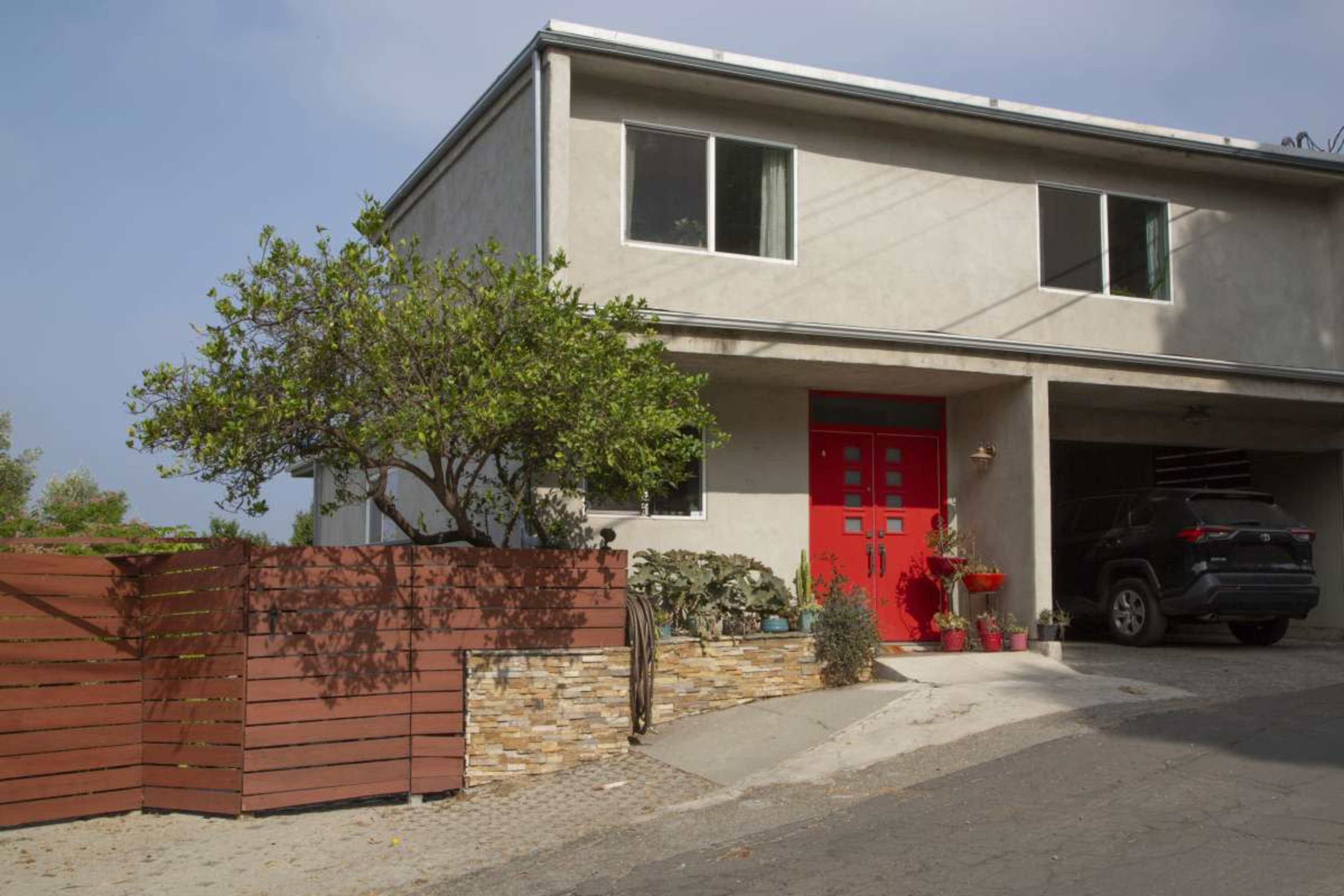 A modern two-story house with a red door and landscaped front yard sits on a sloped driveway.