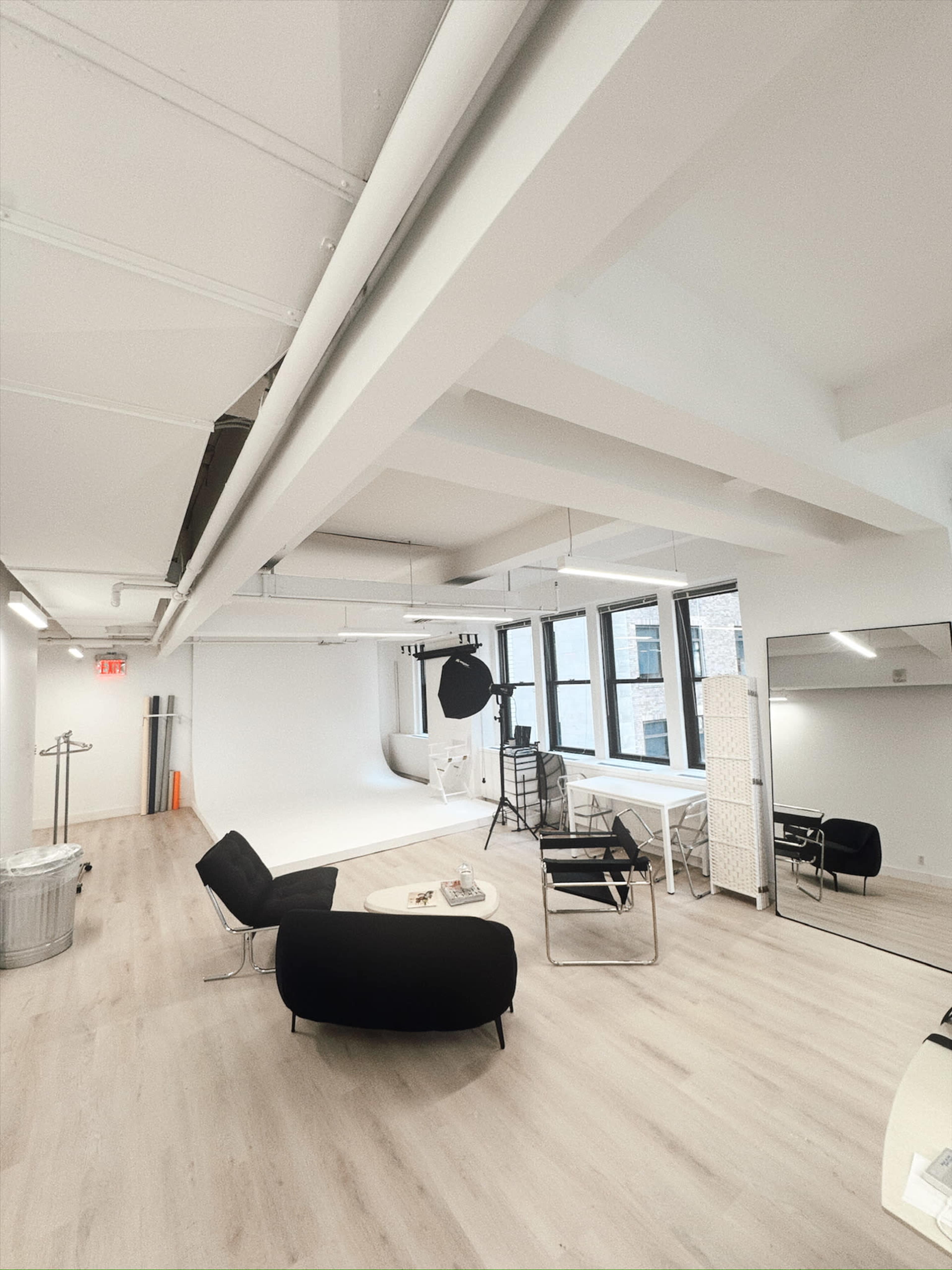 The image shows a spacious photography studio with large windows, a plain backdrop, and contemporary furniture arranged throughout the room.