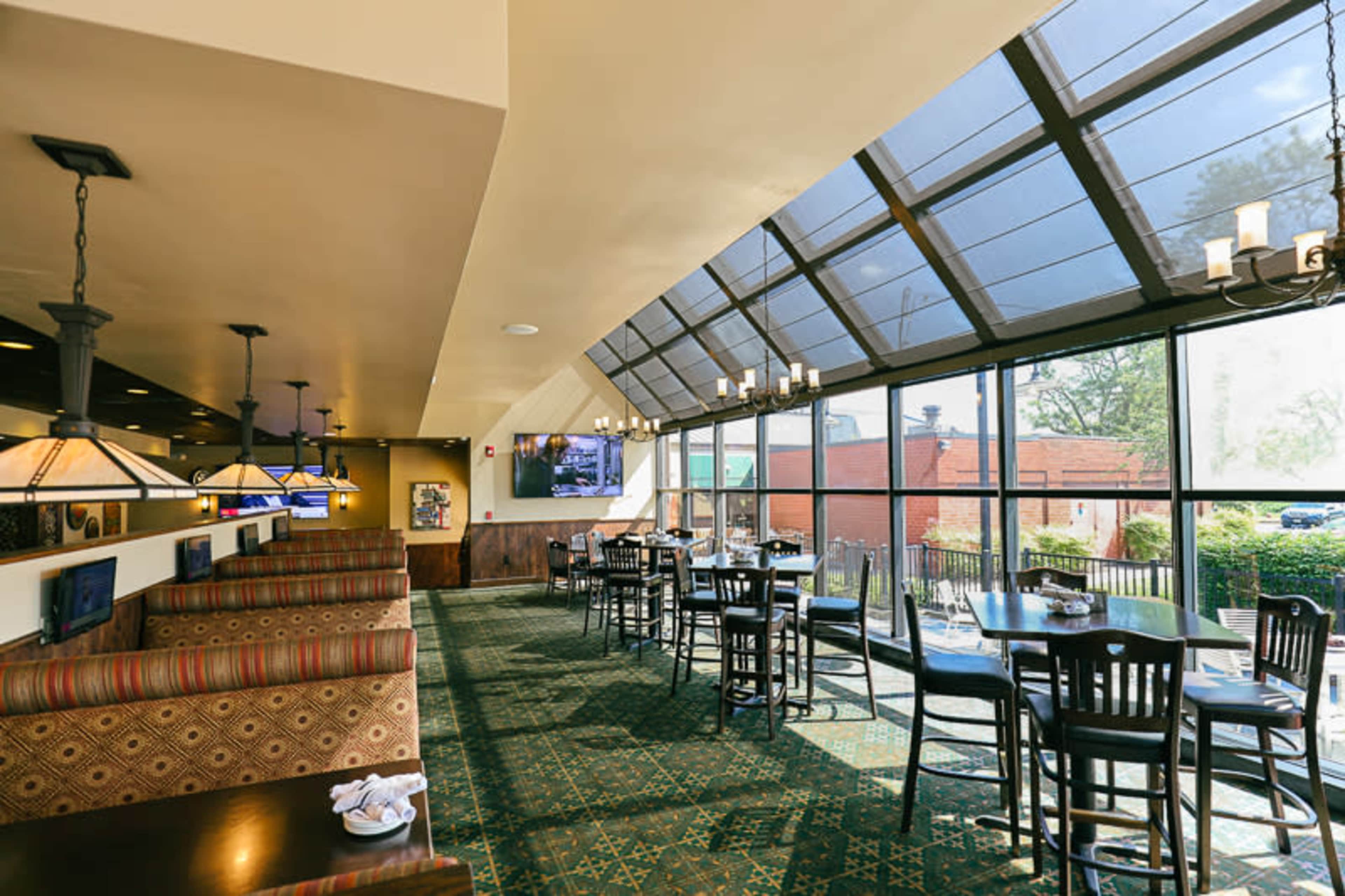The interior of a restaurant featuring large windows, booths along the walls, and several tables arranged in the dining area.