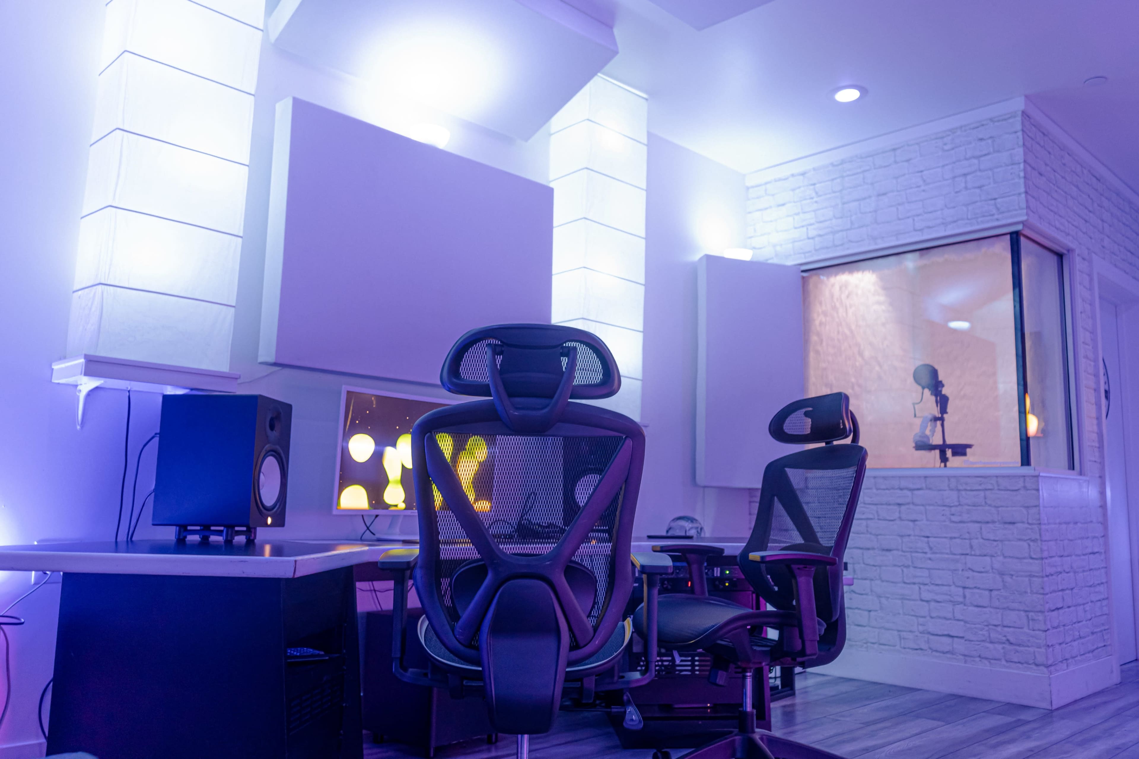 A modern music studio features soundproof walls, a recording booth, and ergonomic chairs set in a soft blue and purple lighting.