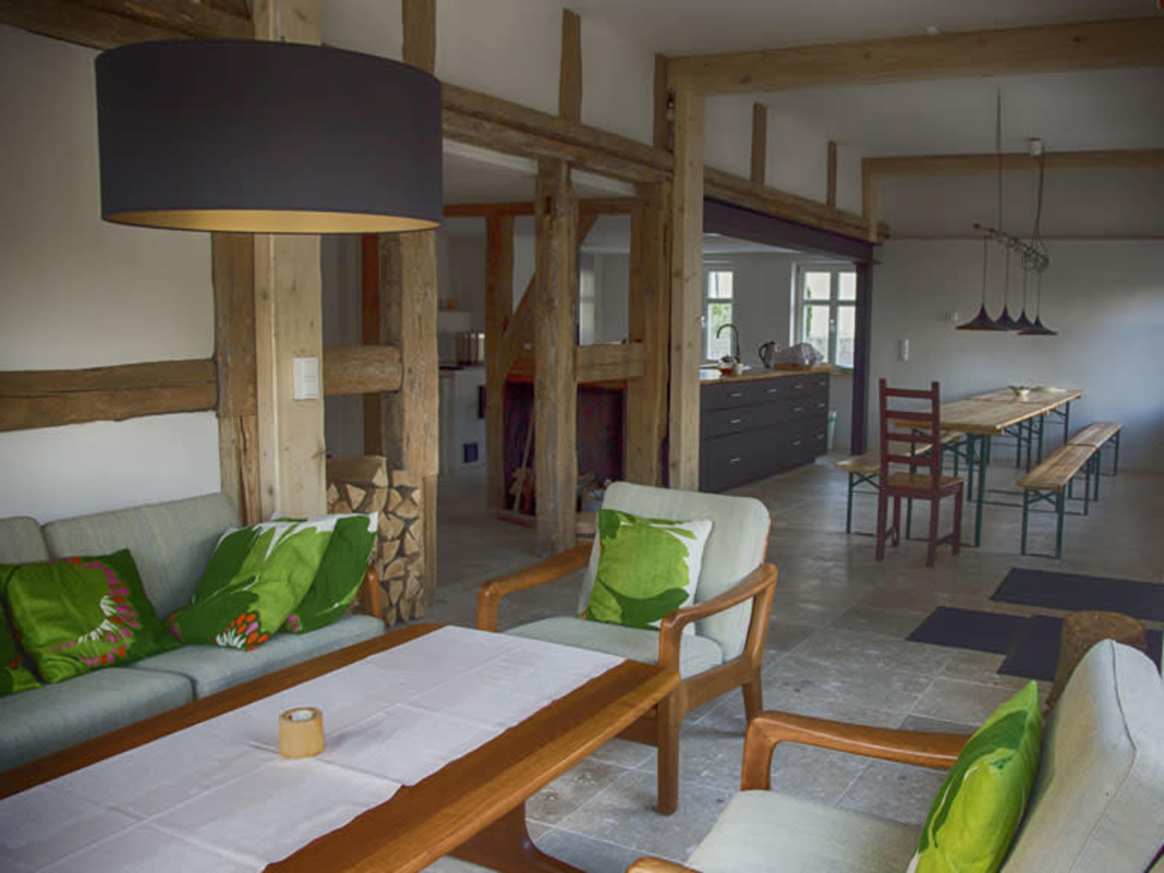 A stylish interior living space featuring wooden beams, a dining table with chairs, and a seating area with green accent pillows.