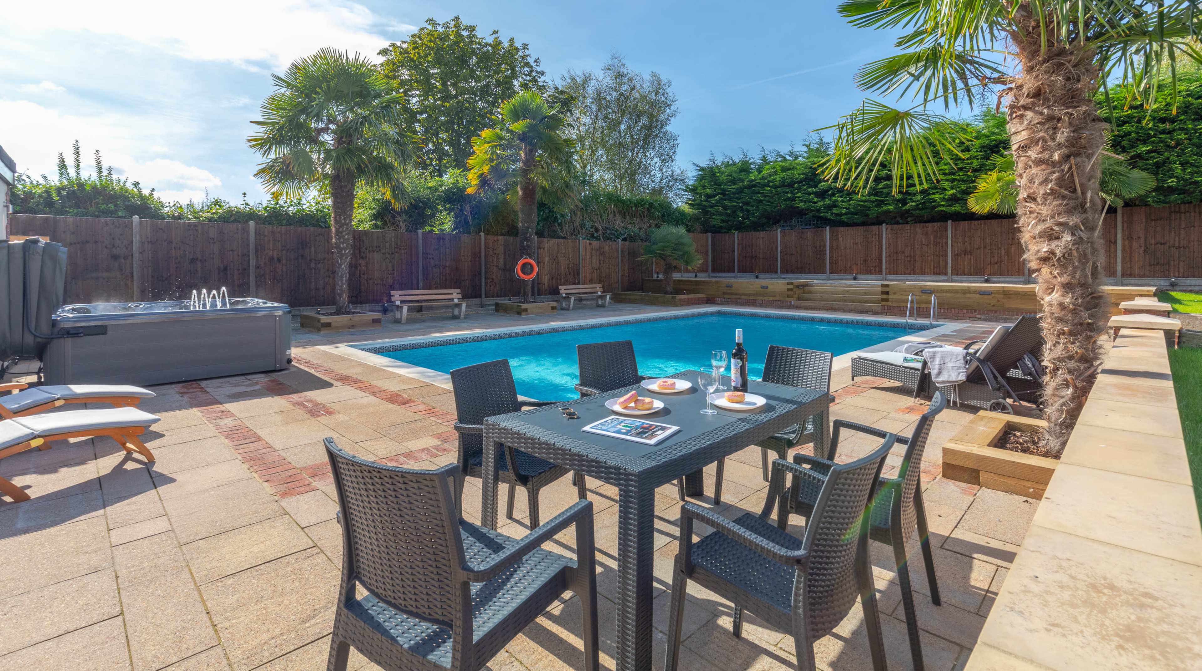A backyard pool area with a swimming pool surrounded by lounge chairs, palm trees, and a patio dining set.