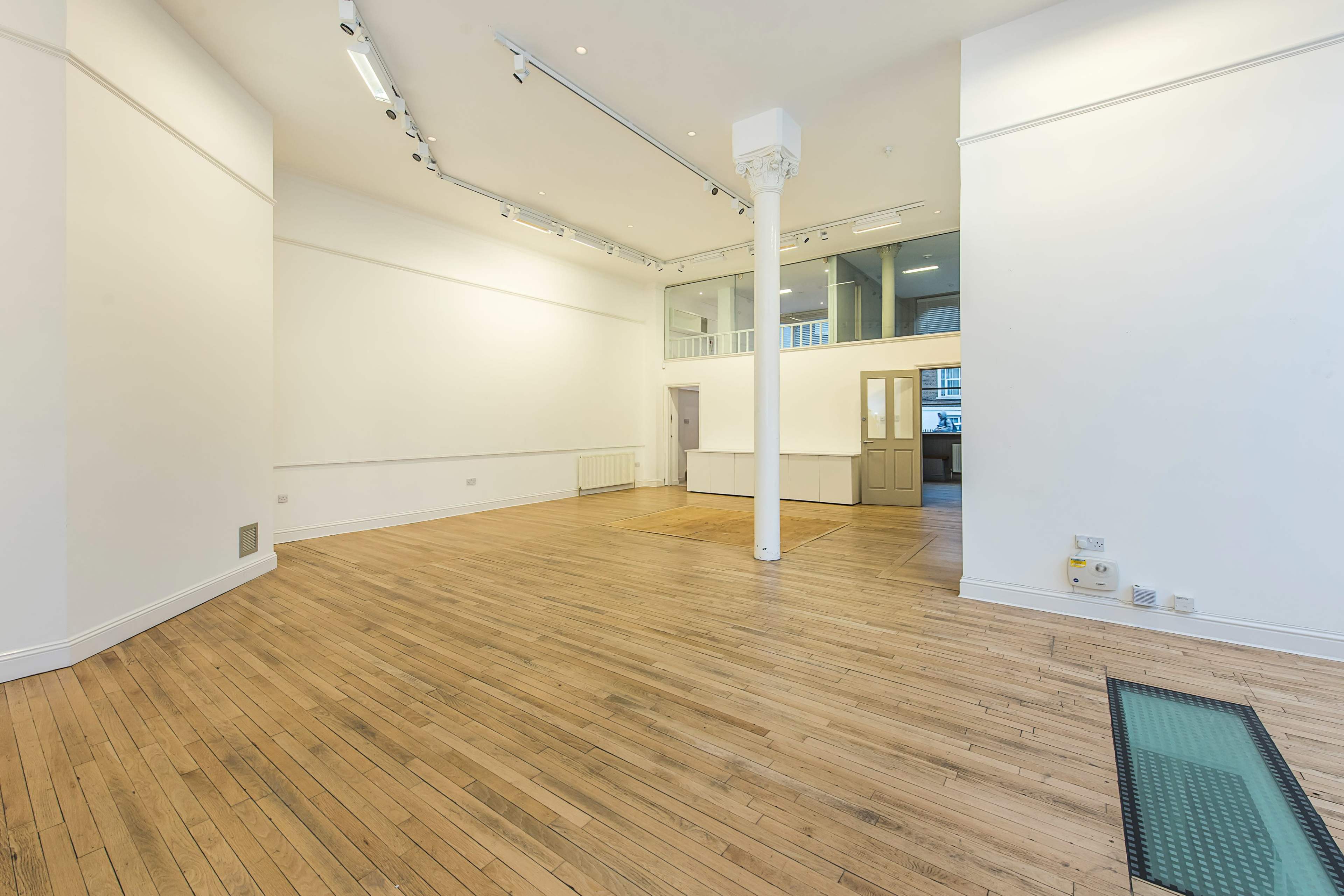 A spacious, empty room with wooden flooring, white walls, and large windows.