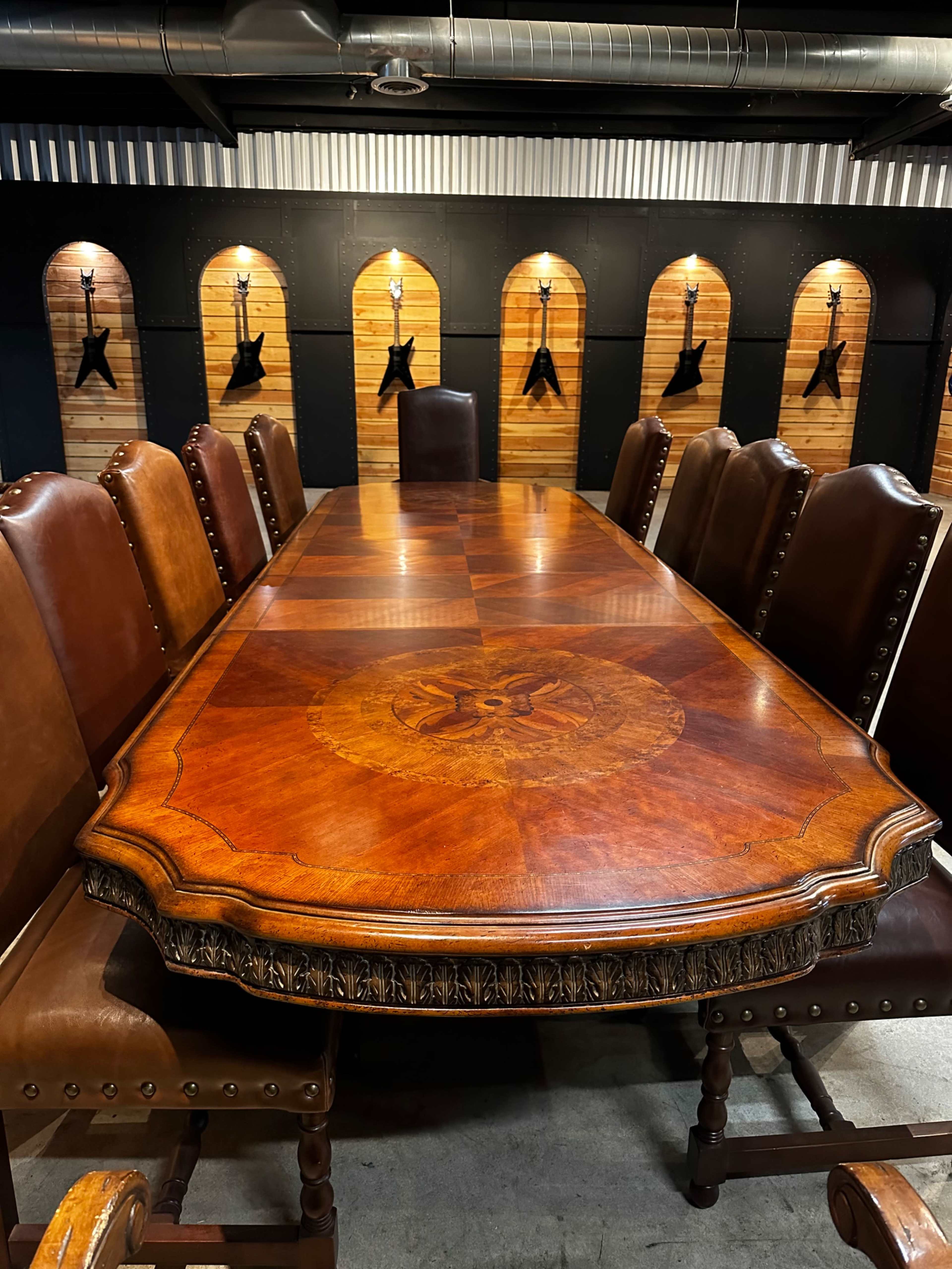 A large, ornate wooden conference table surrounded by leather chairs, set against a backdrop of wooden panels with mounted objects.