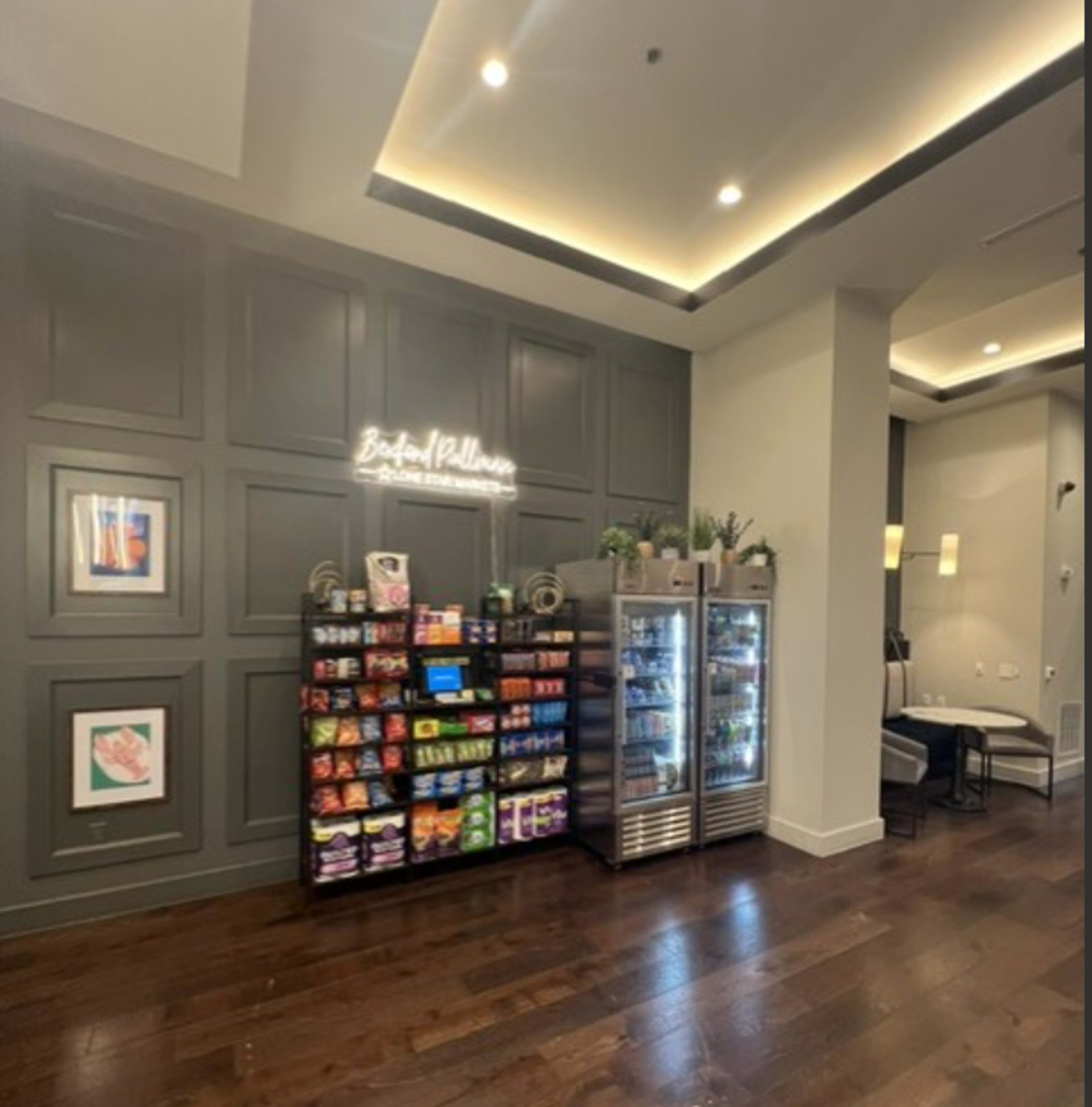 The image shows a lobby area featuring a snack display with various food items and a glass refrigerator beside it, complemented by modern decor and ambient lighting.
