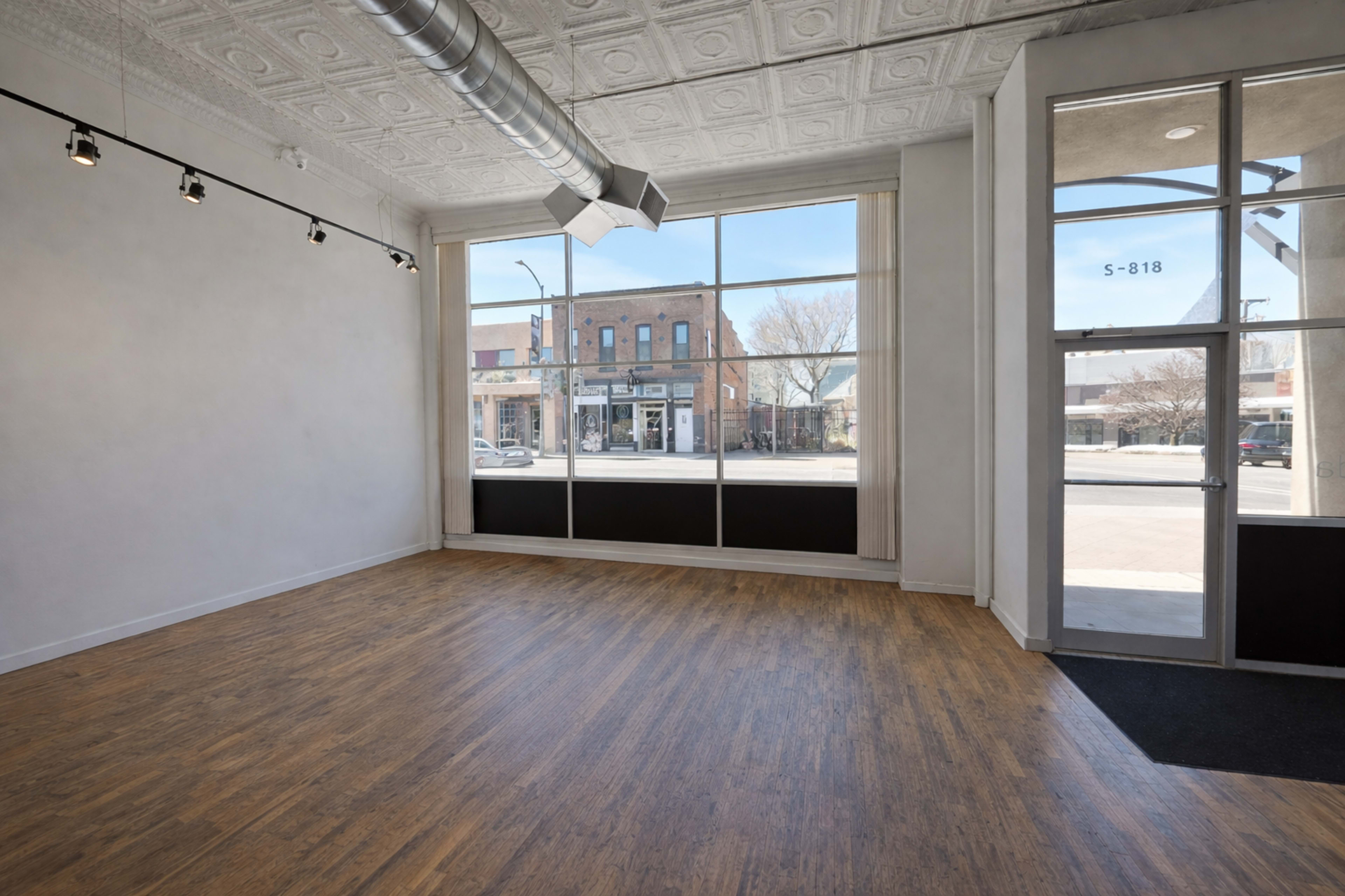 The image shows an empty retail space with large windows facing a street, featuring wooden flooring and exposed ceiling ducts.