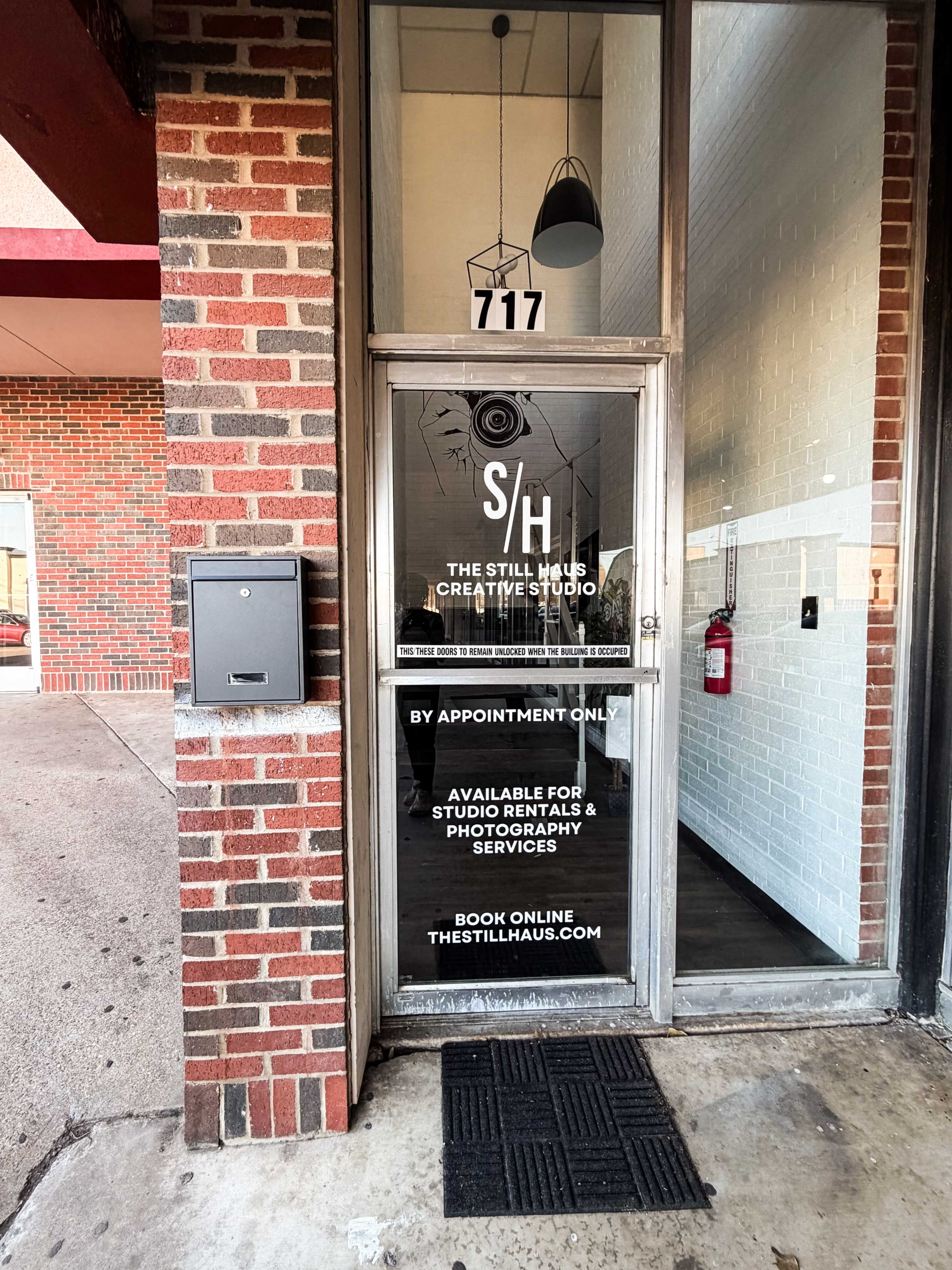The image shows the entrance of a creative studio labeled "The Still Haus," with a glass door featuring a sign indicating it is by appointment only and offering studio rentals and photography services.