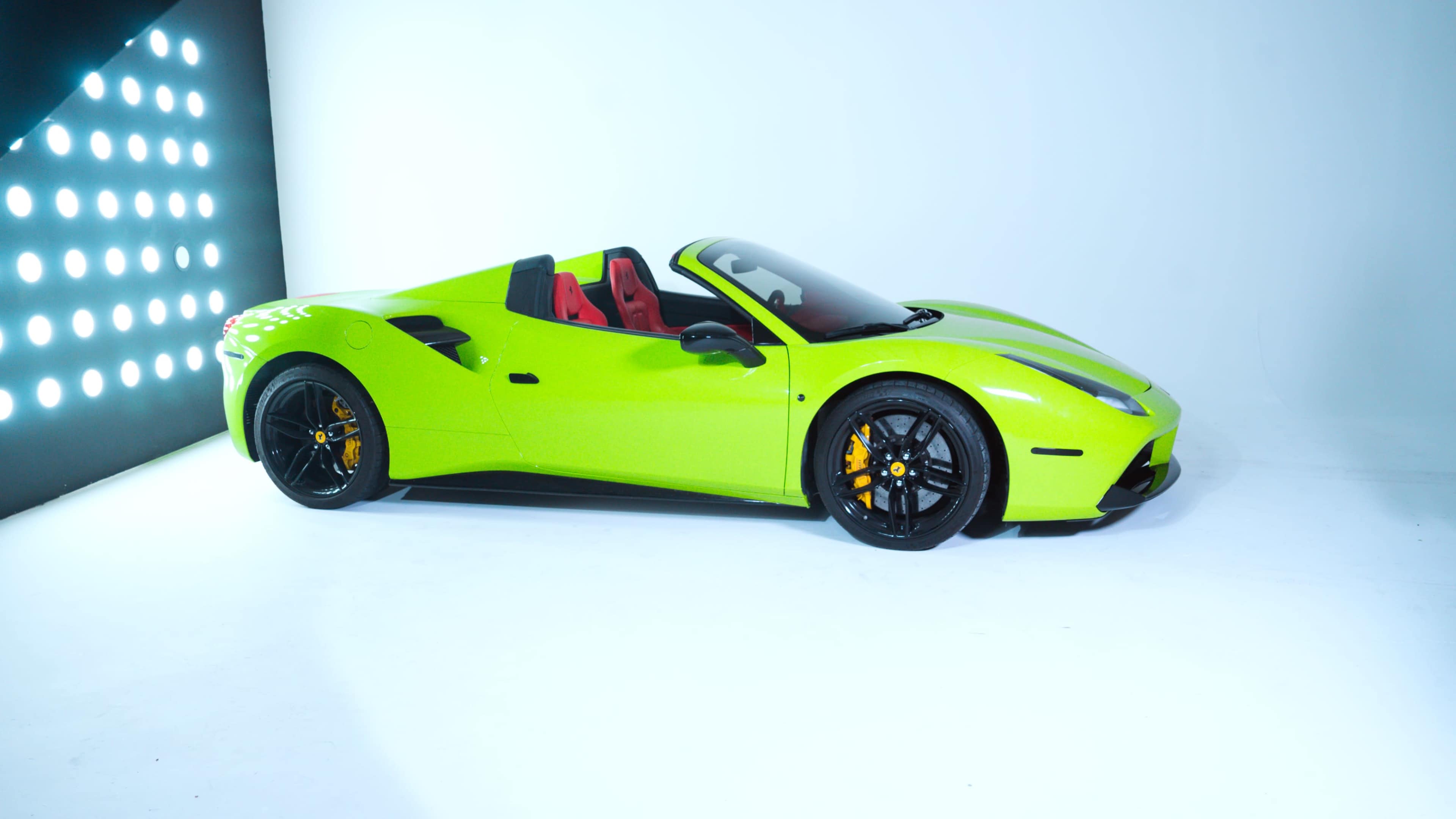 A bright green sports car with black wheels and red interior is positioned against a minimalistic white backdrop with light panels.