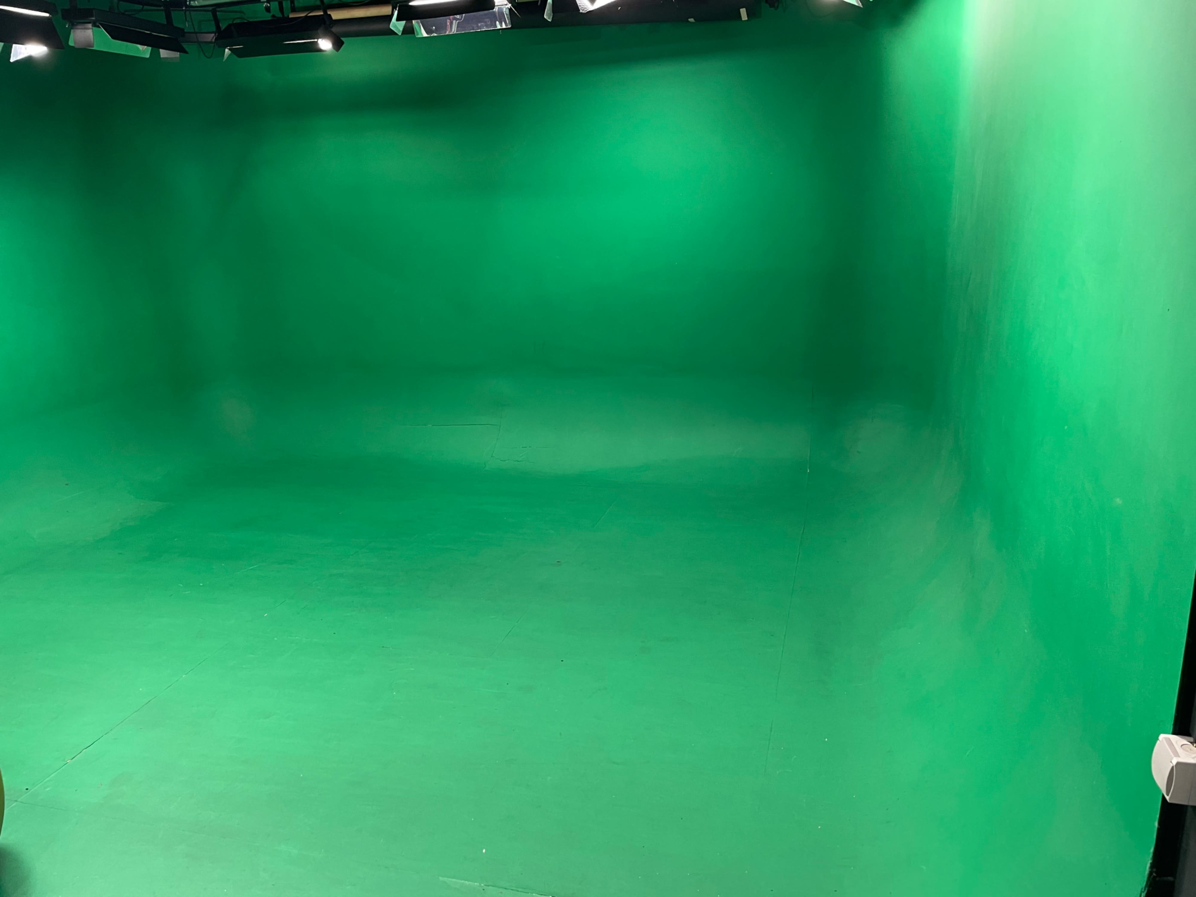 The image shows an empty green screen studio with a smooth, green floor and walls.