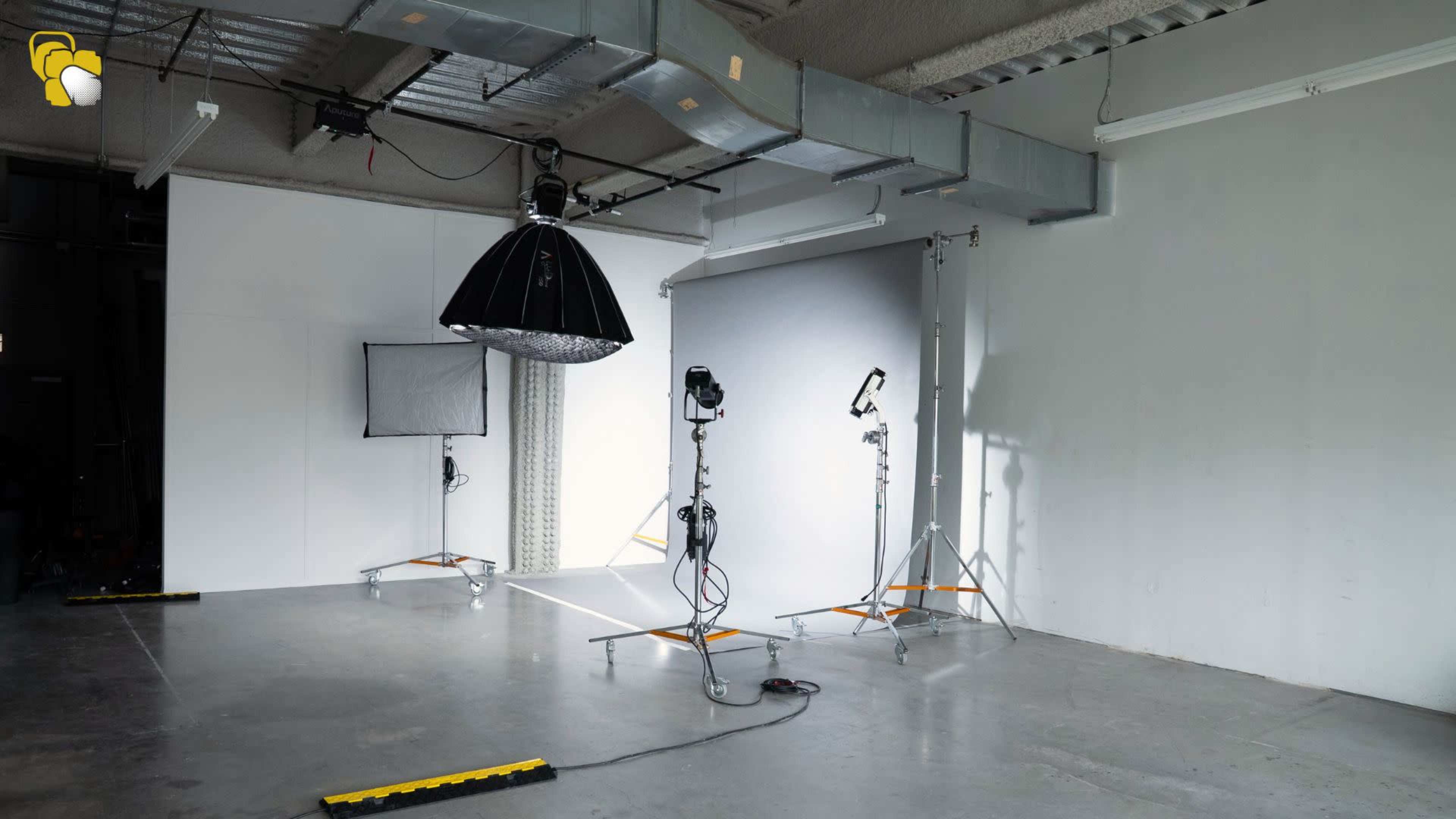 The image shows a photography studio with various lighting equipment, including softboxes and a large umbrella, set up against a backdrop.