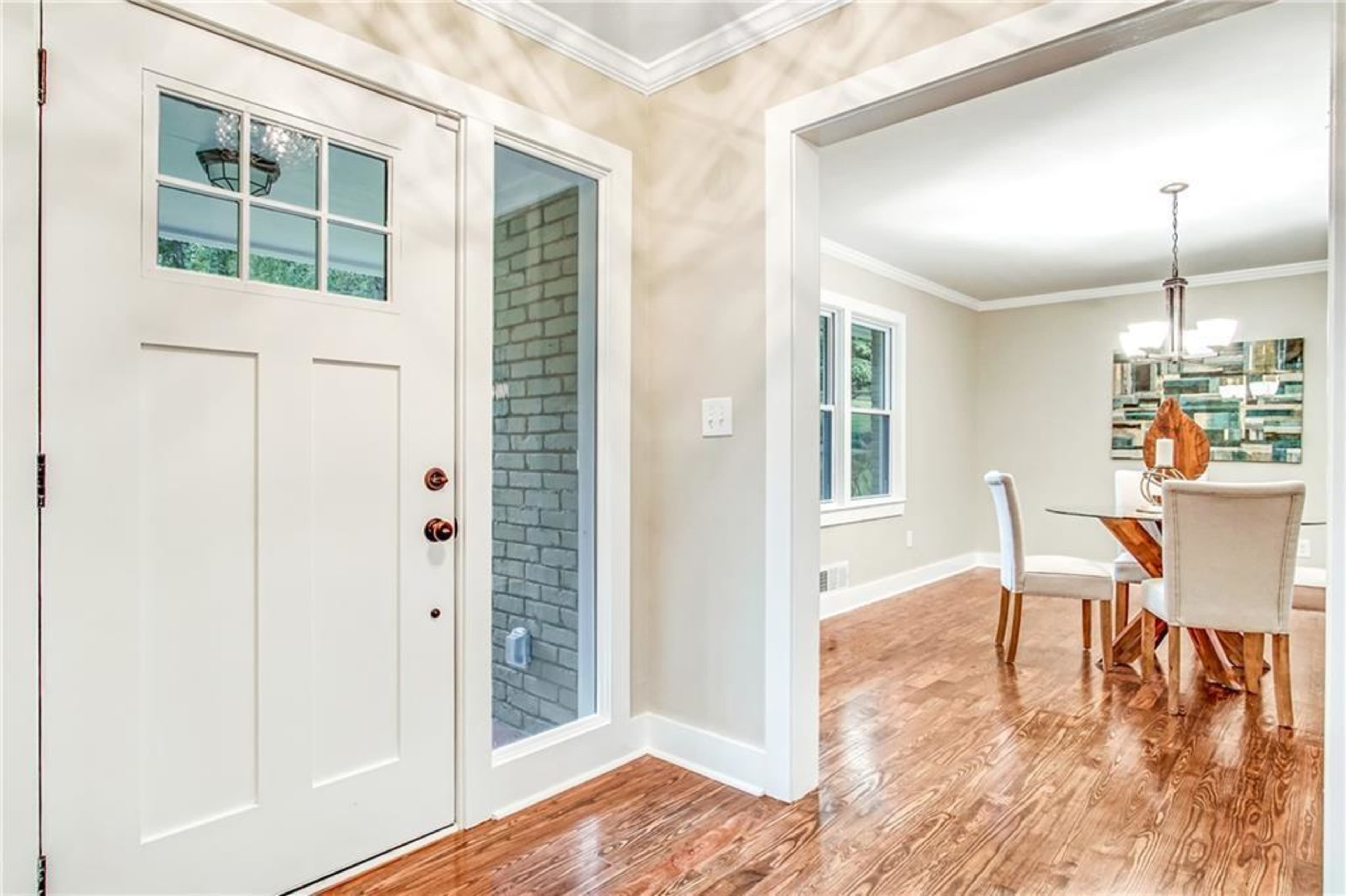 An entryway with a white front door and a view into a dining area featuring a table and chairs.