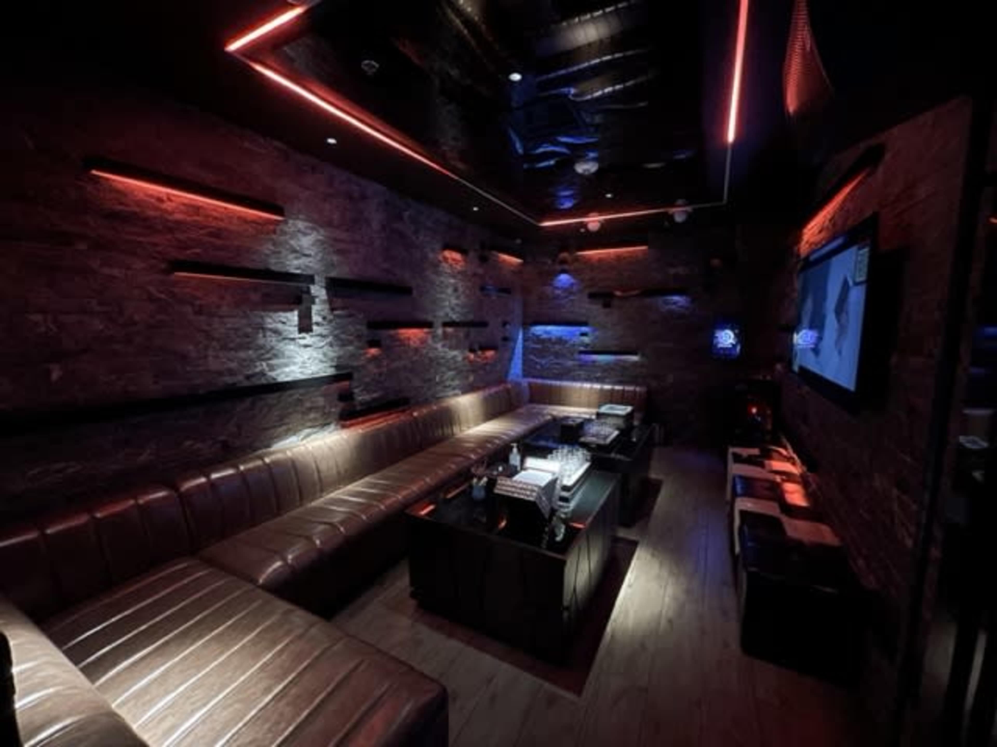 A dimly lit lounge with a long leather seating area and a television mounted on the wall.