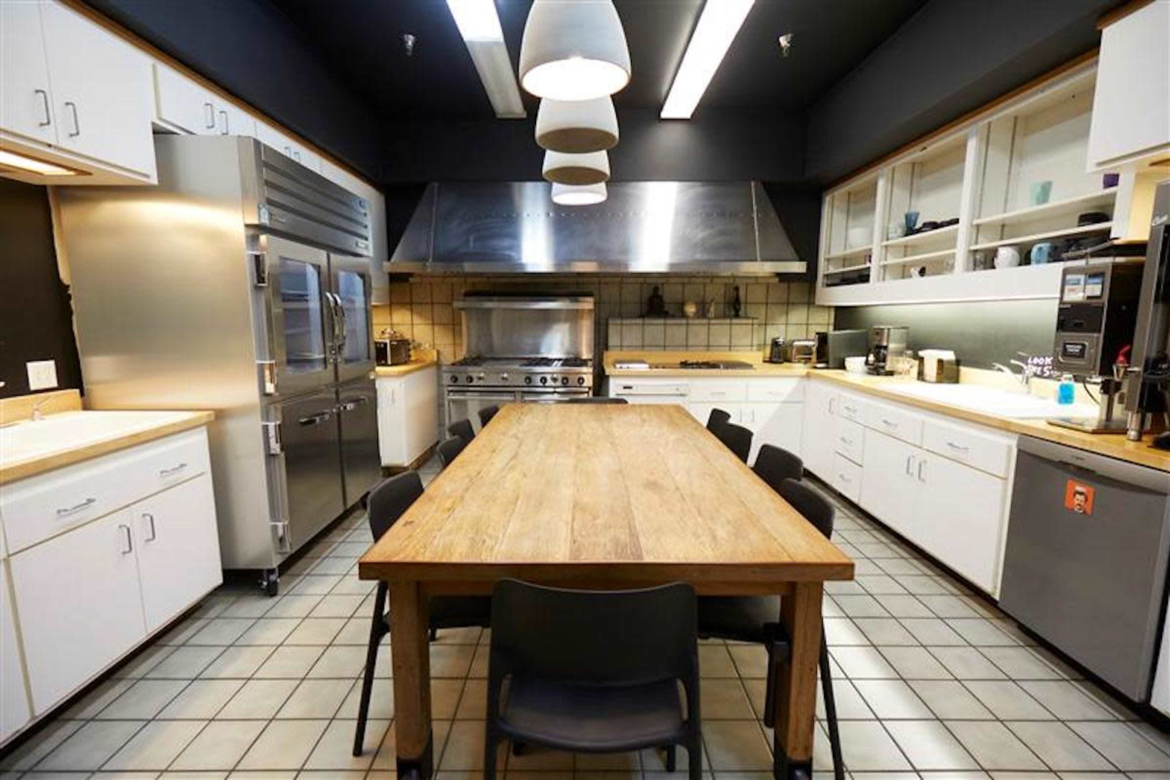 A modern kitchen features stainless steel appliances, a large wooden table, and white cabinetry.