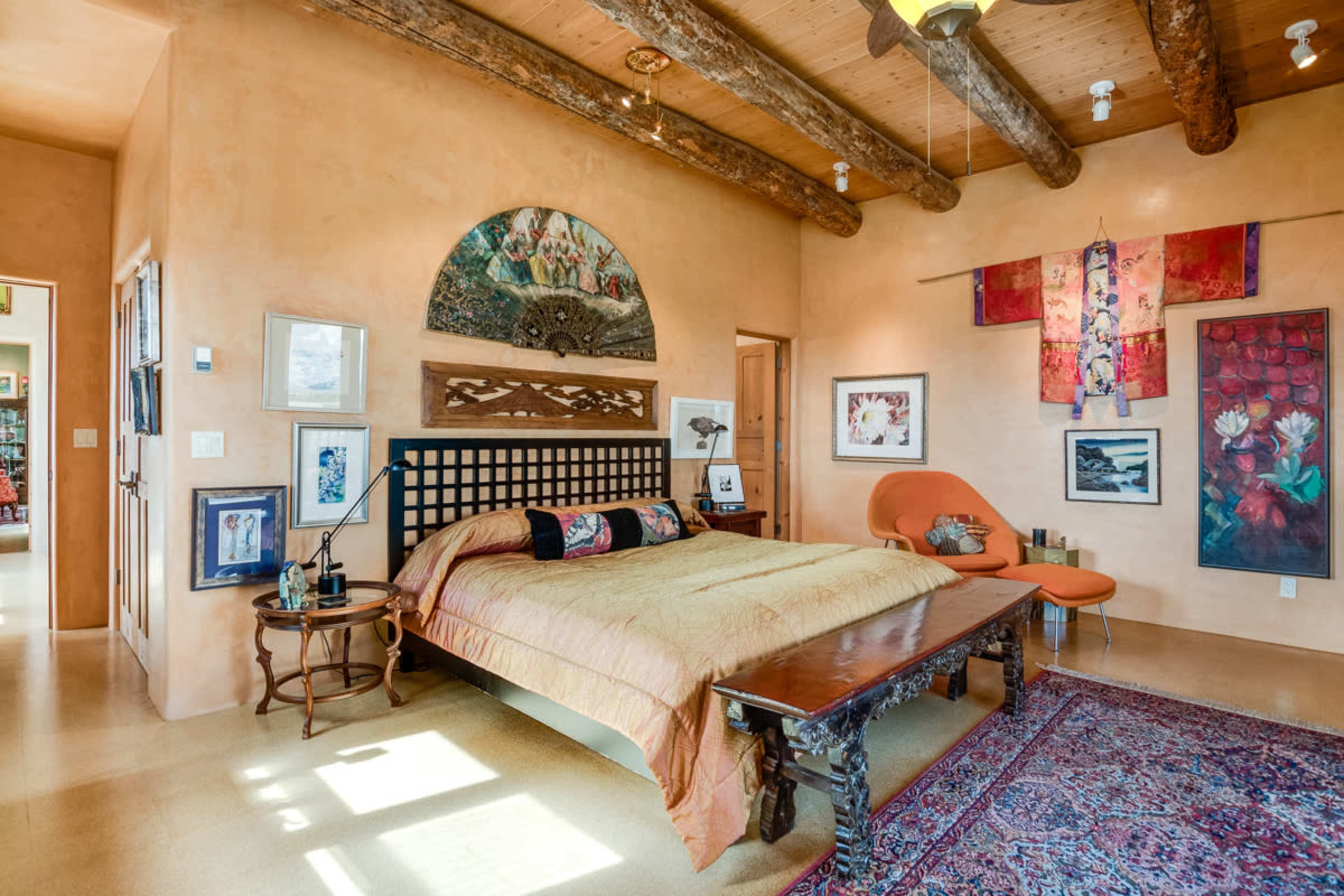 A cozy bedroom featuring a wooden bed with a decorative headboard, orange accent chair, and walls adorned with various artworks.