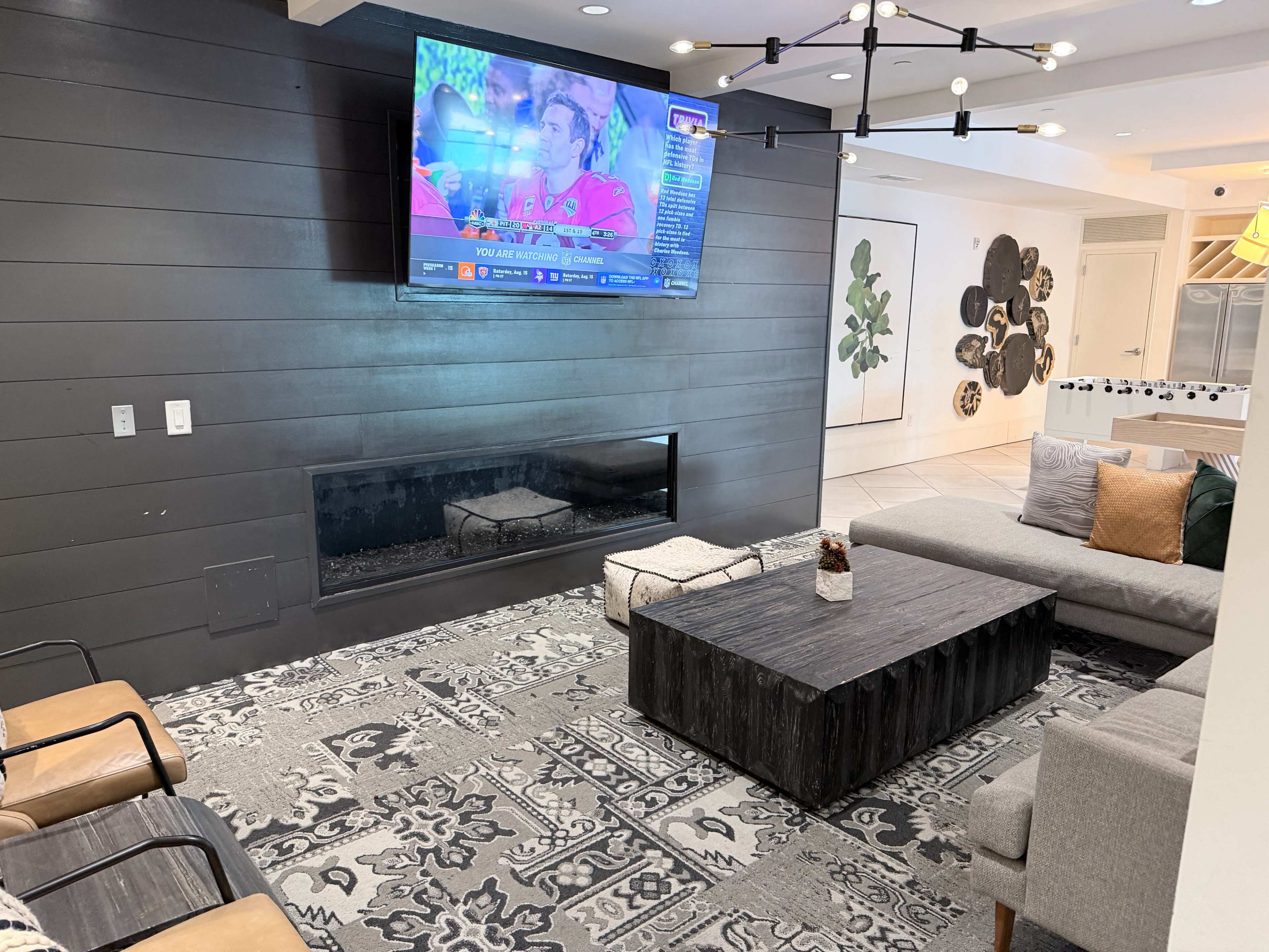 The image shows a modern living room with a wall-mounted television, a rectangular coffee table, a fireplace, and a sectional sofa arranged around a patterned area rug.