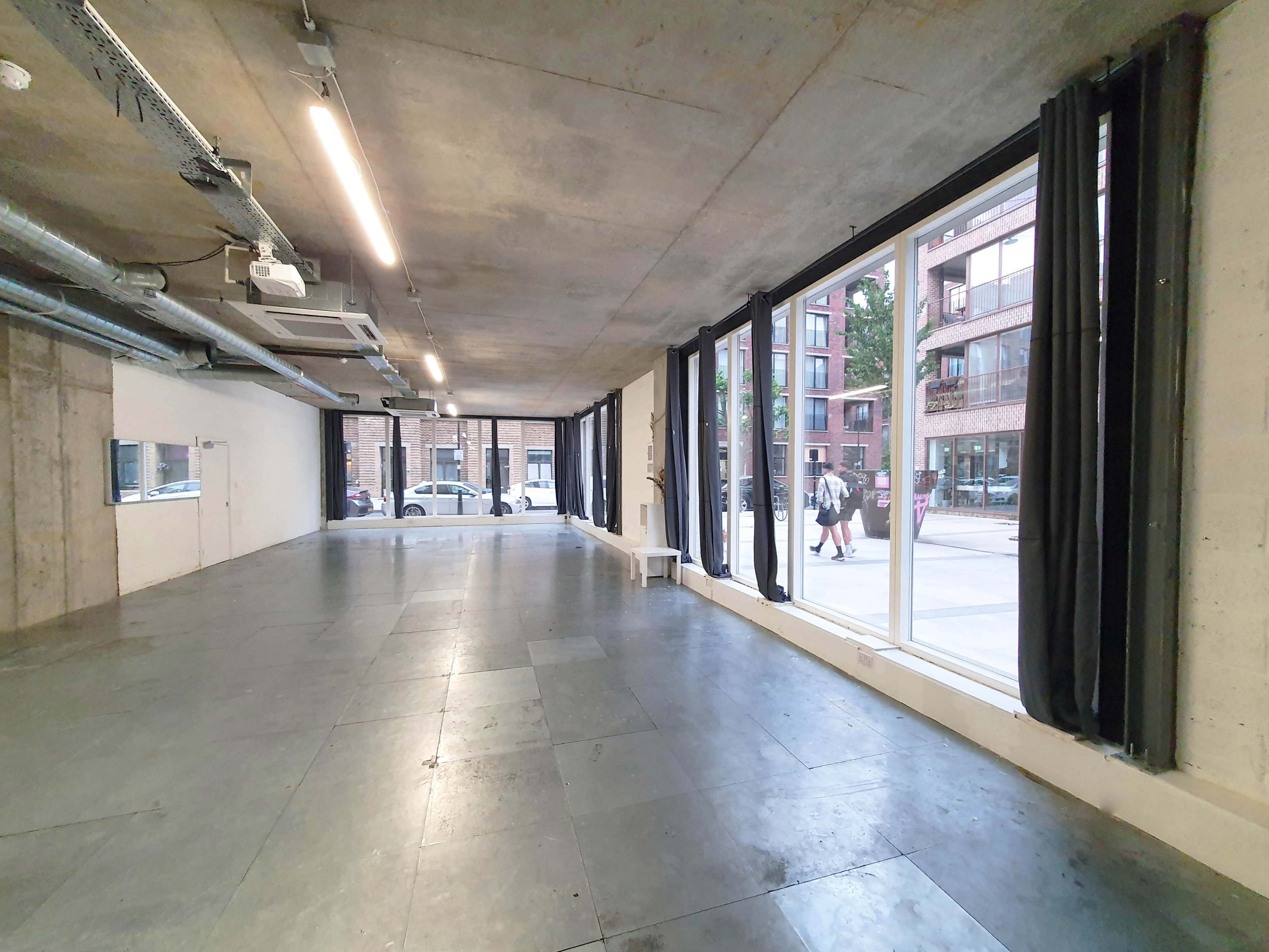 An empty interior space with large windows, concrete walls, and a polished floor.