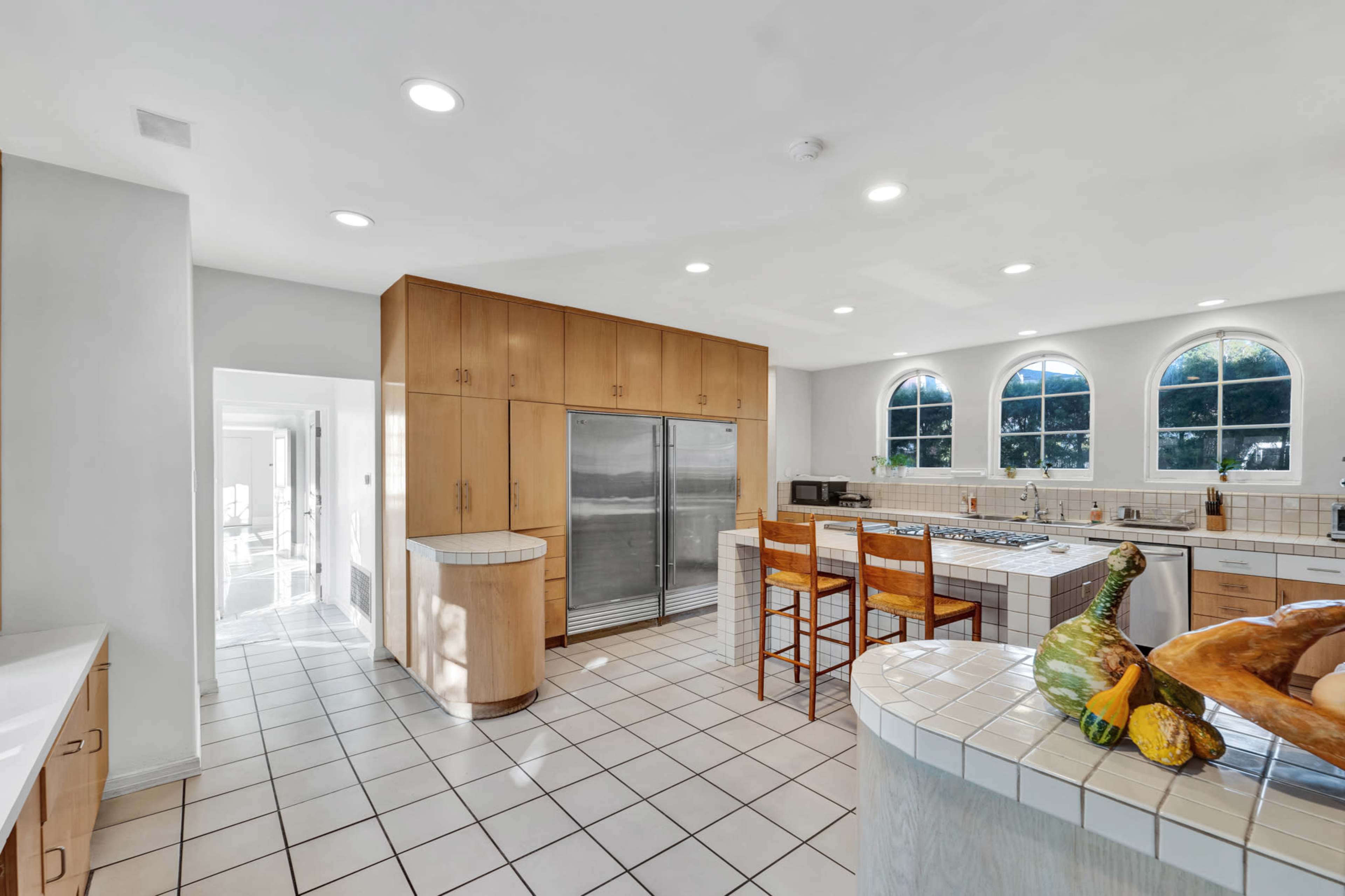 A spacious kitchen features light wood cabinetry, stainless steel appliances, and a tiled island with bar seating.
