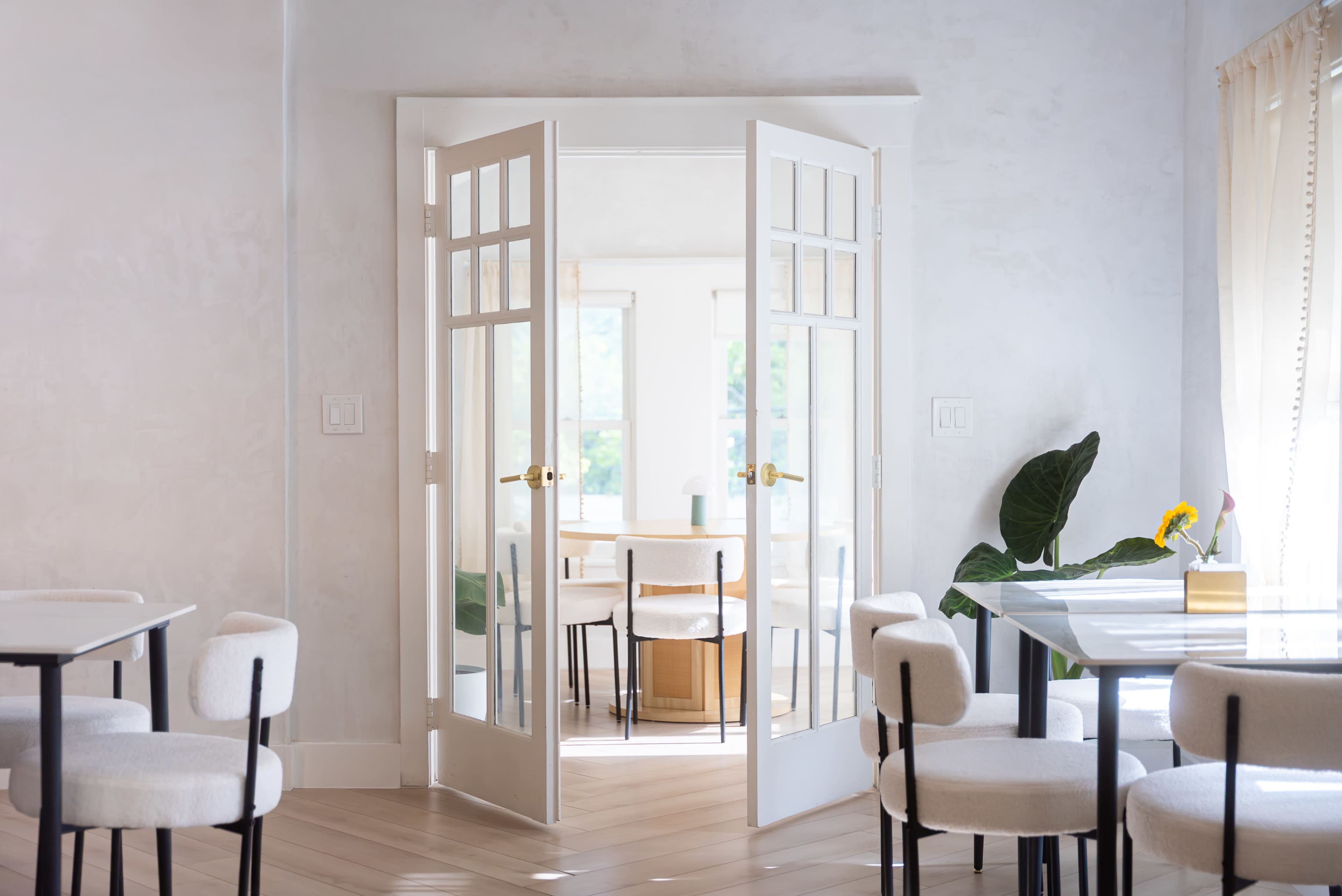 A bright, modern room features open double doors leading to another space, surrounded by minimalist furniture and natural light.