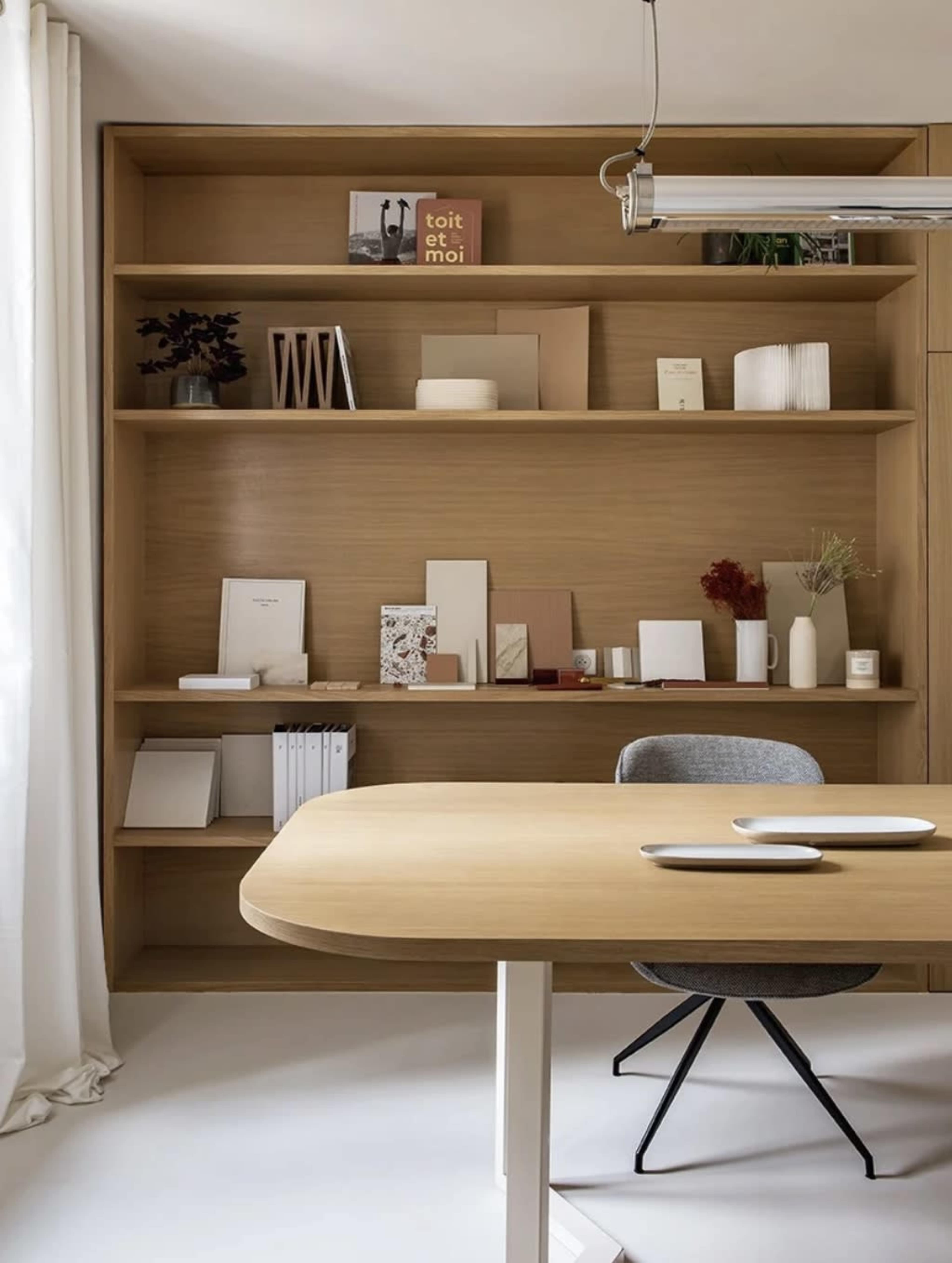 The image shows a minimalist wooden desk in front of a neatly organized shelf filled with various decorative items and stationery.