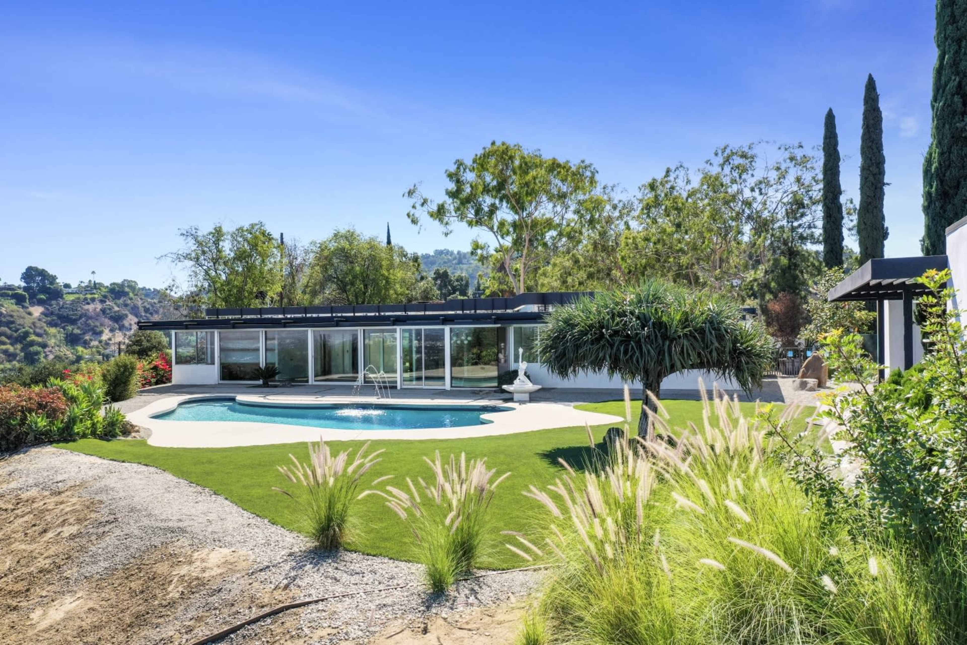A modern single-story house with a swimming pool and landscaped garden surrounded by trees and shrubs.