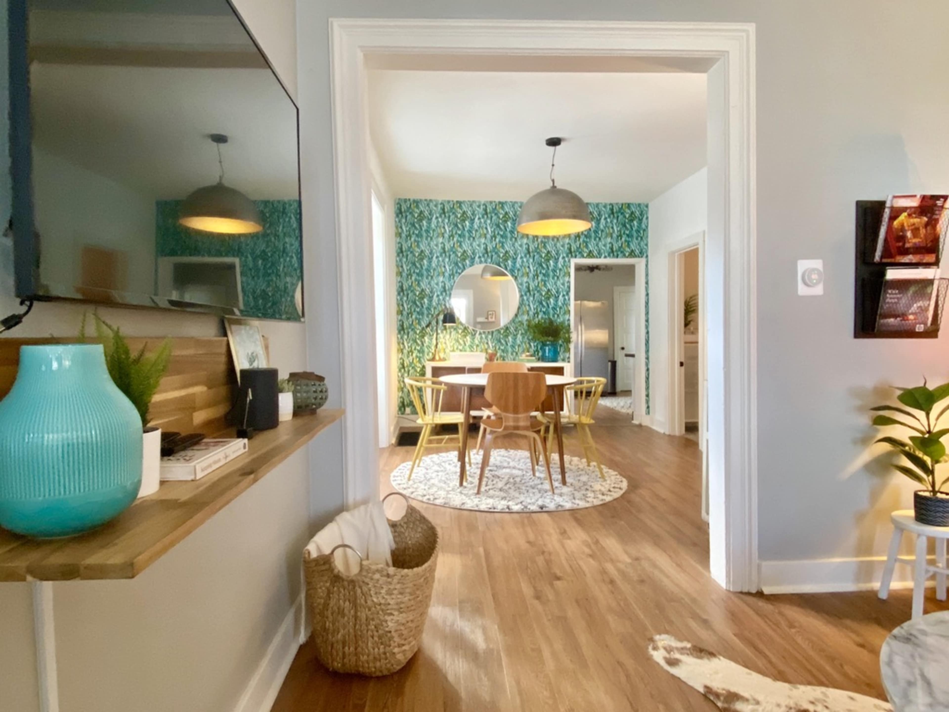 A view through an archway reveals a dining area with a round table and a colorful wallpaper backdrop.
