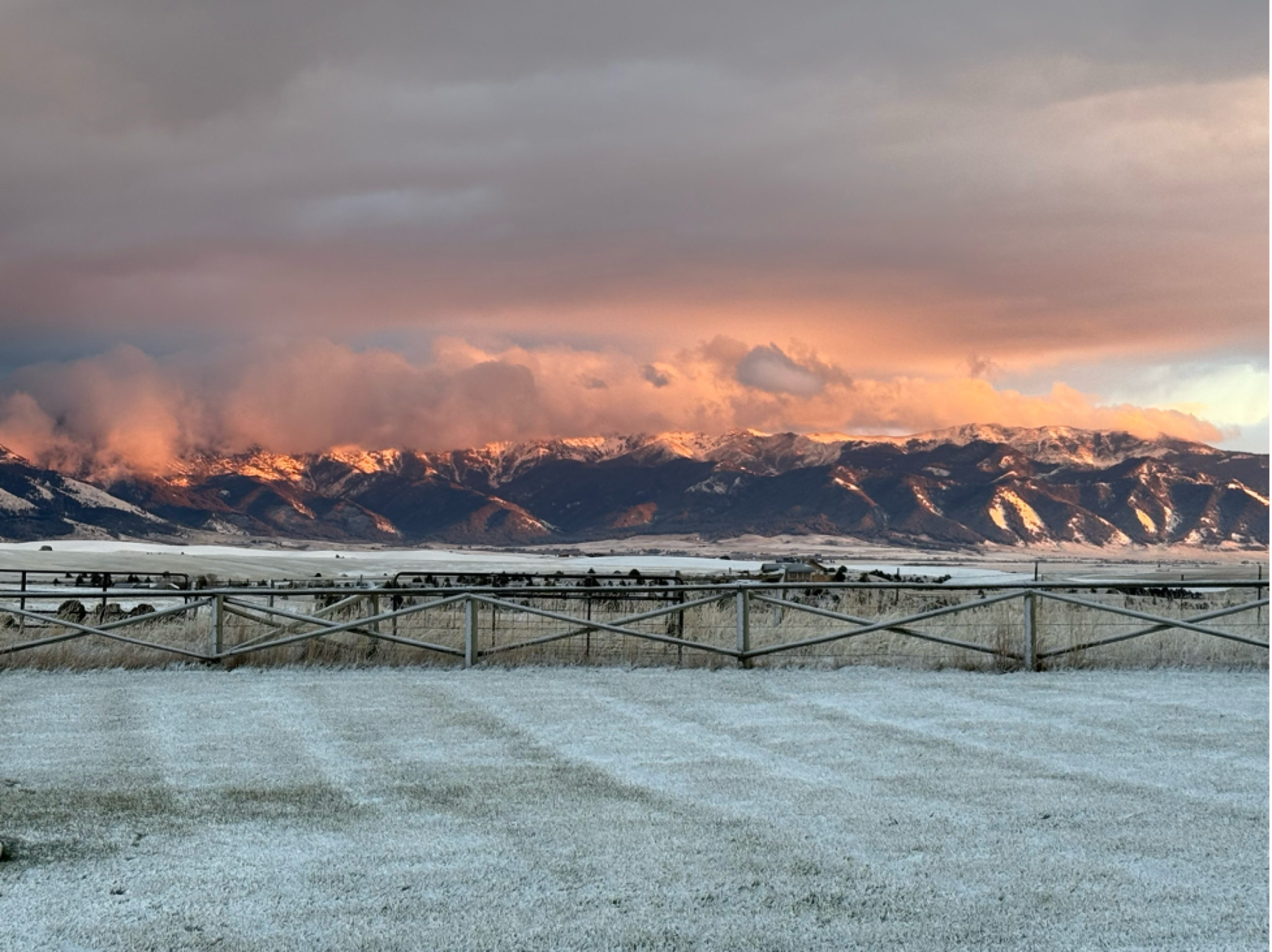 The image shows a snow-covered field with mountains in the background illuminated by a warm sunset.