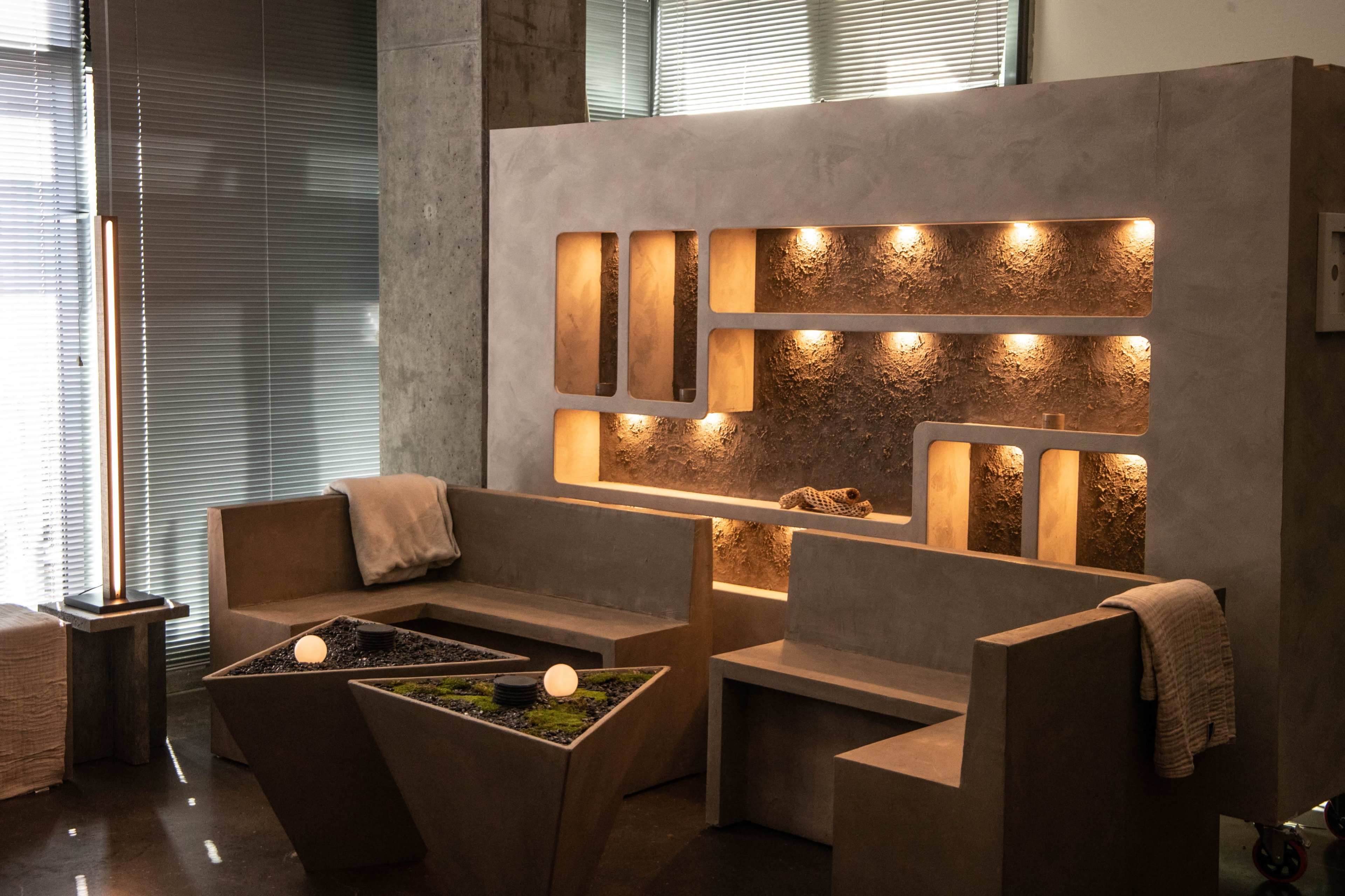 The image shows a modern interior space featuring a concrete seating arrangement and a textured wall with integrated lighting.