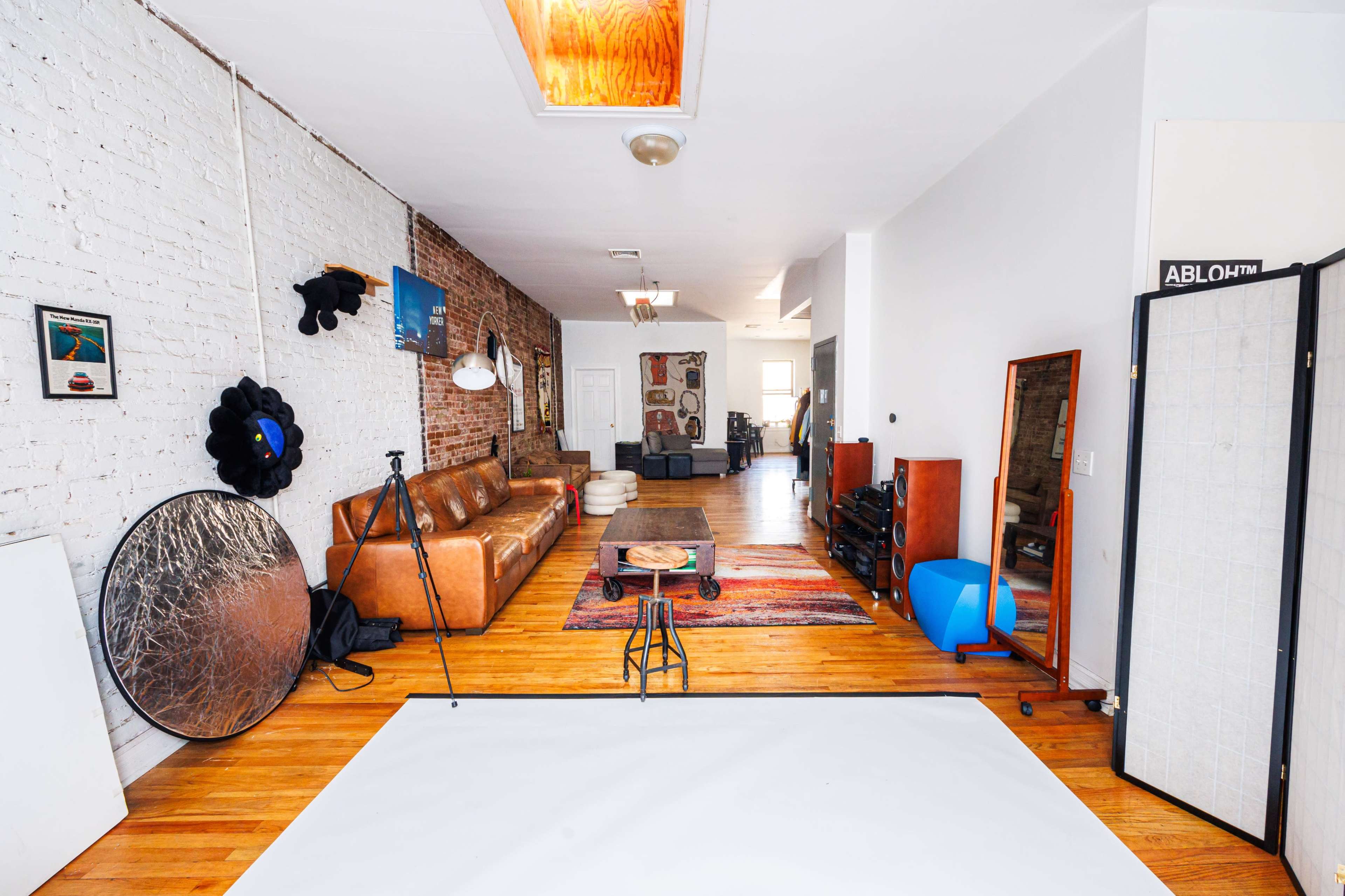 A spacious room featuring a brown leather sofa, a colorful area rug, and various decorative items against exposed brick and white walls.
