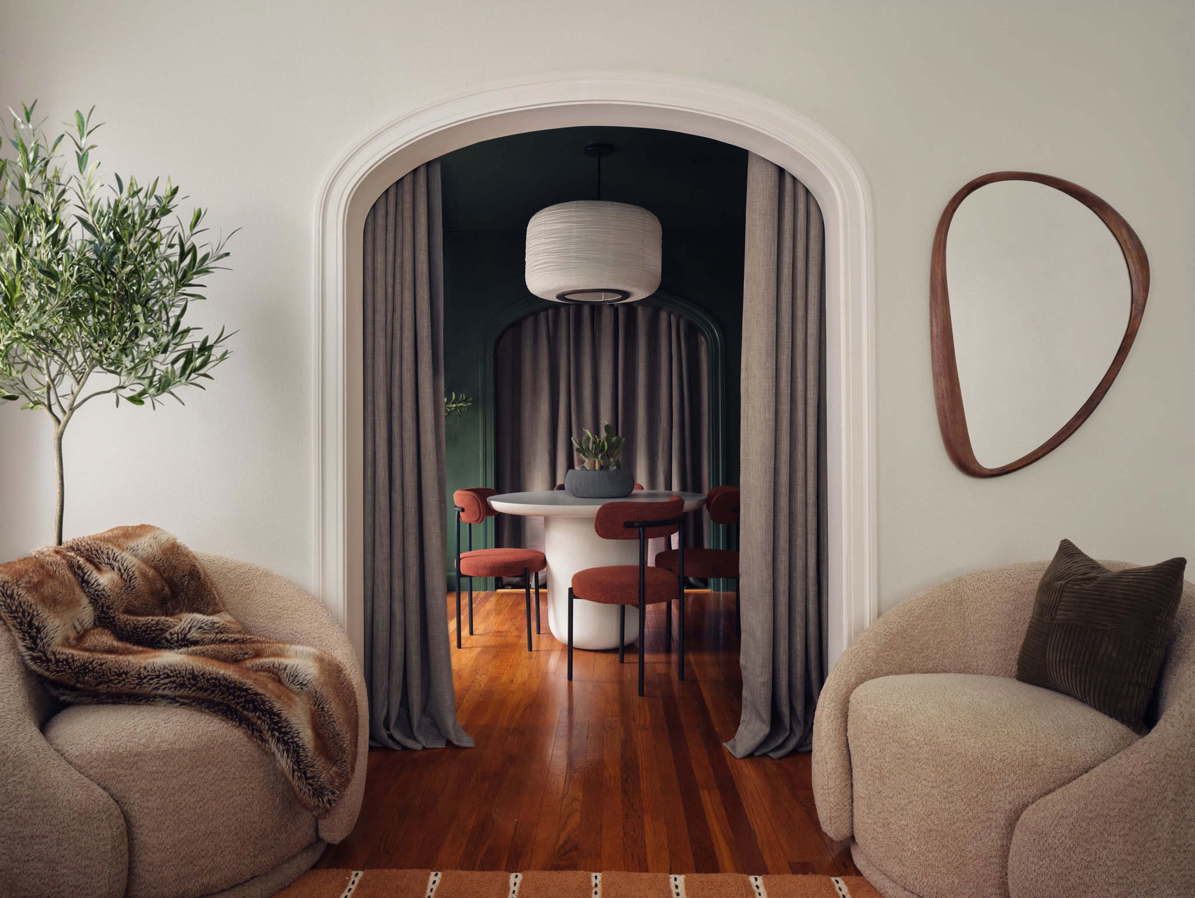 A cozy living space features two rounded armchairs, an archway with curtains, and a dining area with a circular table and four chairs.