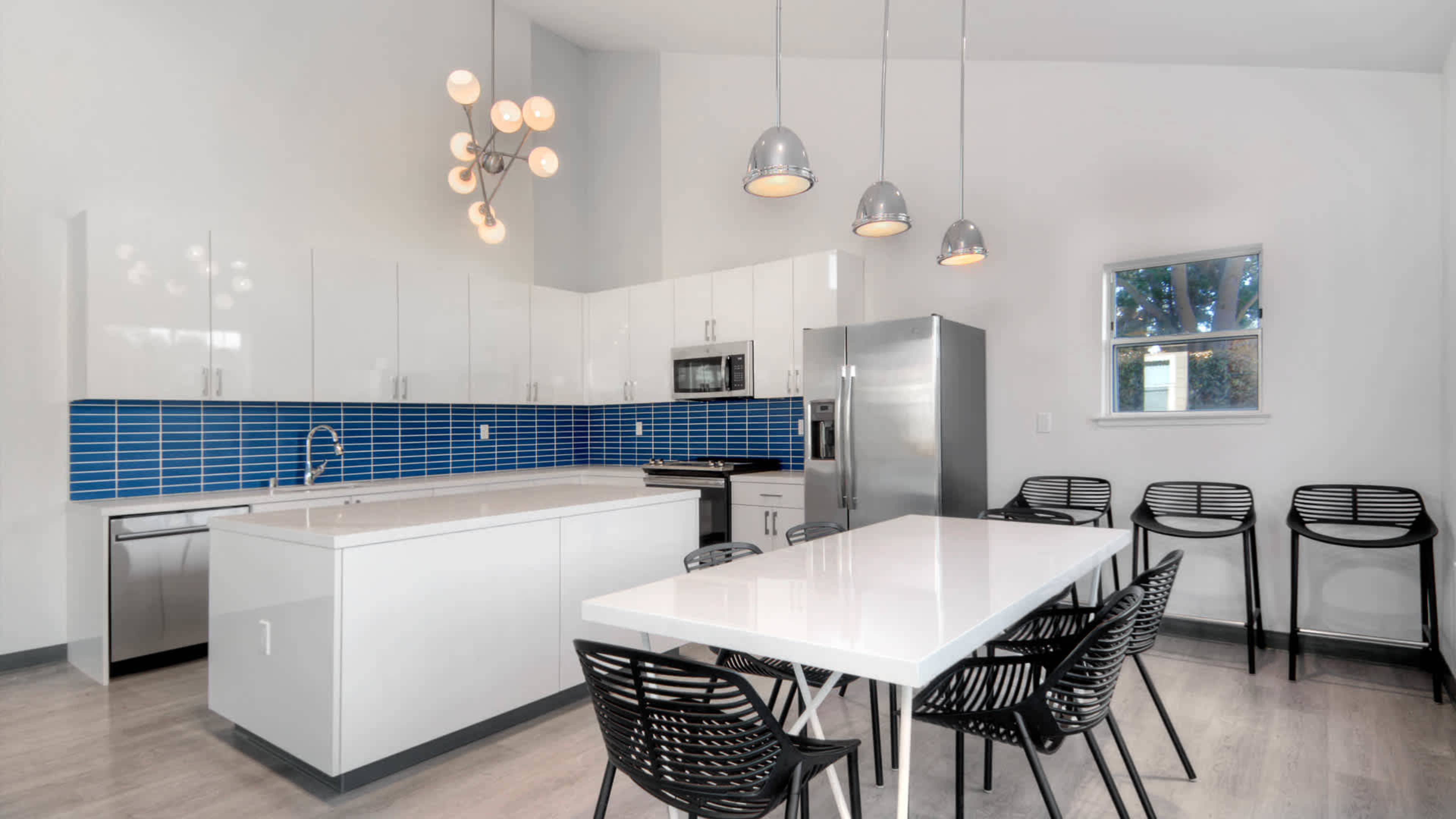 A modern kitchen with a blue tiled backsplash, white cabinets, a large island, and a dining table with black chairs.