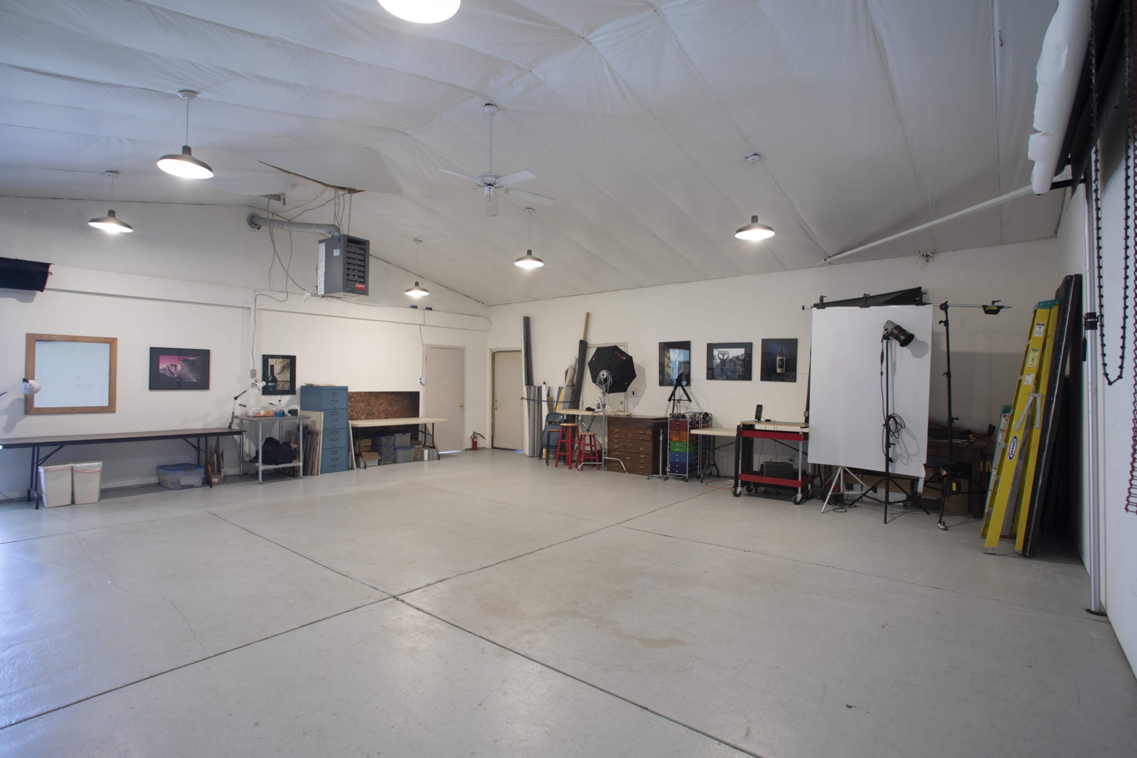 A large interior space with a high ceiling, featuring various equipment, a white backdrop, and several lighting fixtures on the walls.