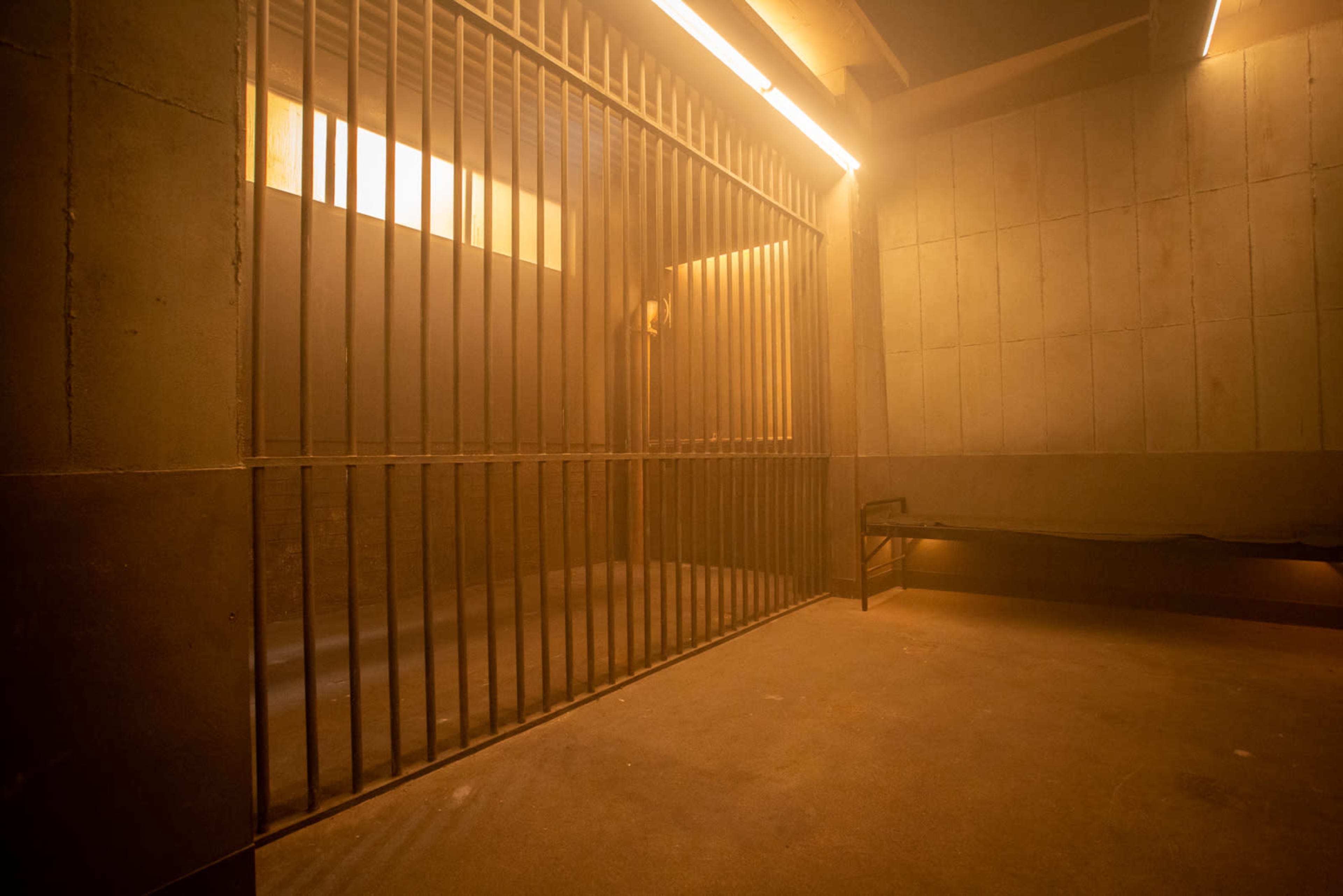A dimly lit room with a barred cell and a bench against the wall.