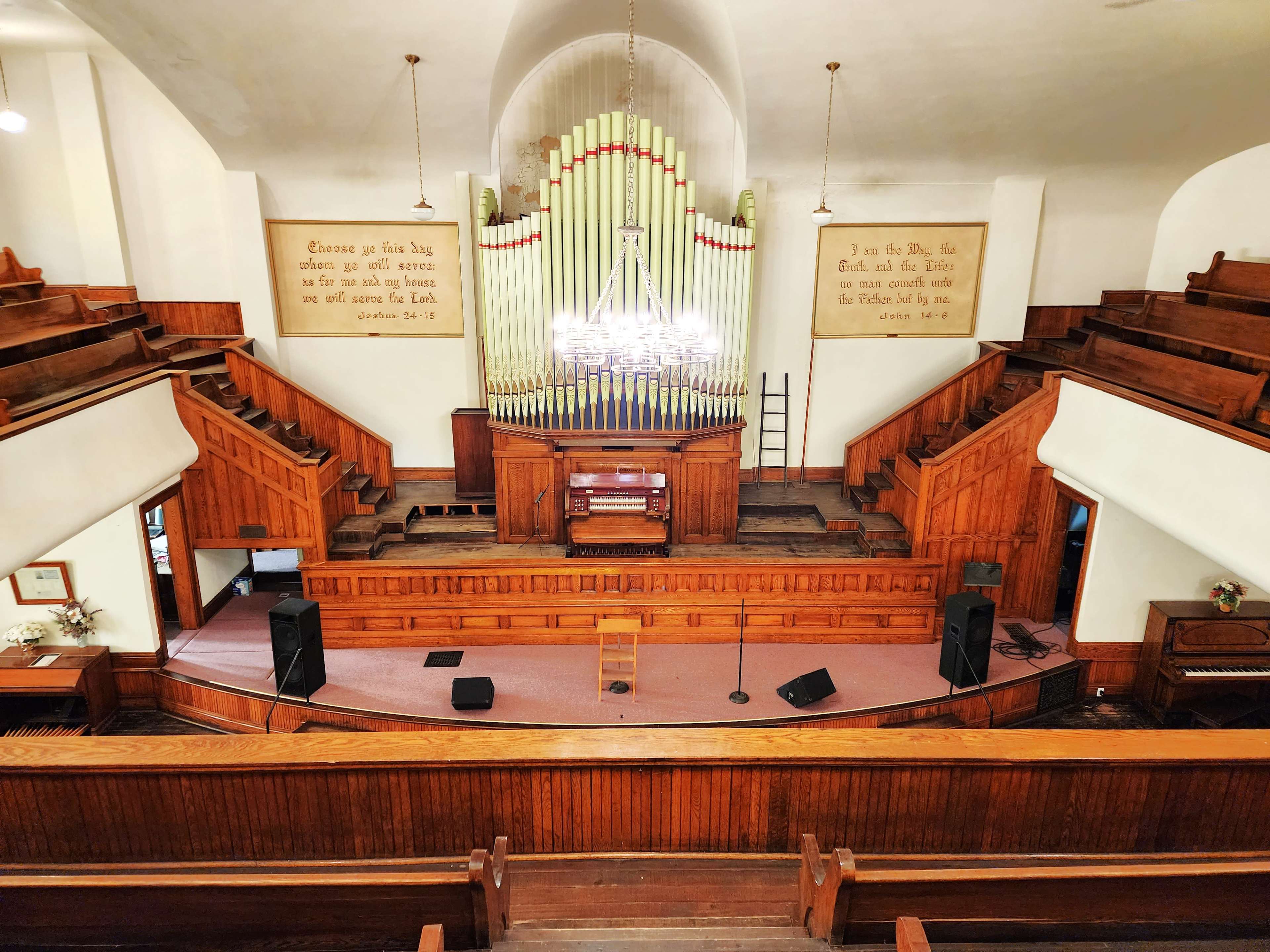 The interior of a church featuring wooden pews, an organ at the front, and two large wall inscriptions.