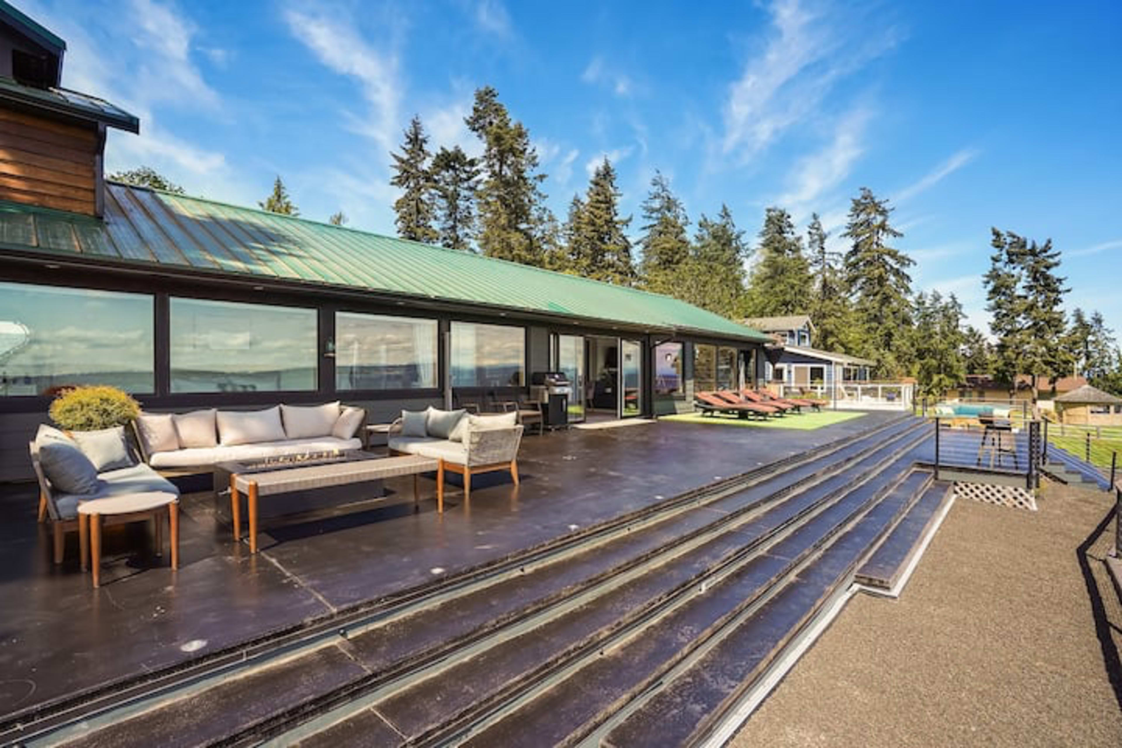 A spacious outdoor patio features a seating area with a sofa and coffee table, overlooking a lush landscape and surrounded by trees.