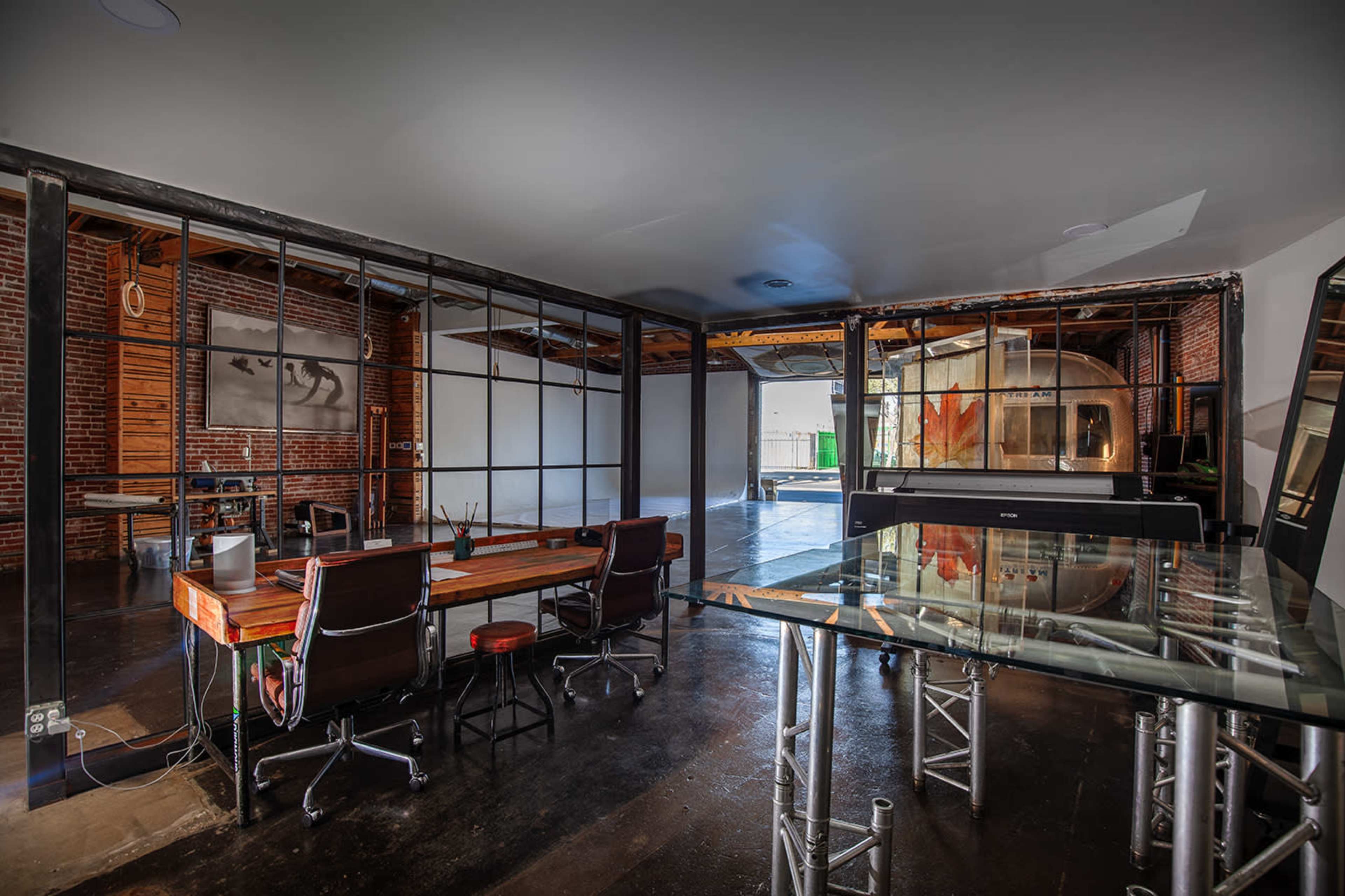A spacious, modern office interior featuring brick walls, glass partitions, a wooden desk, and metal furniture.