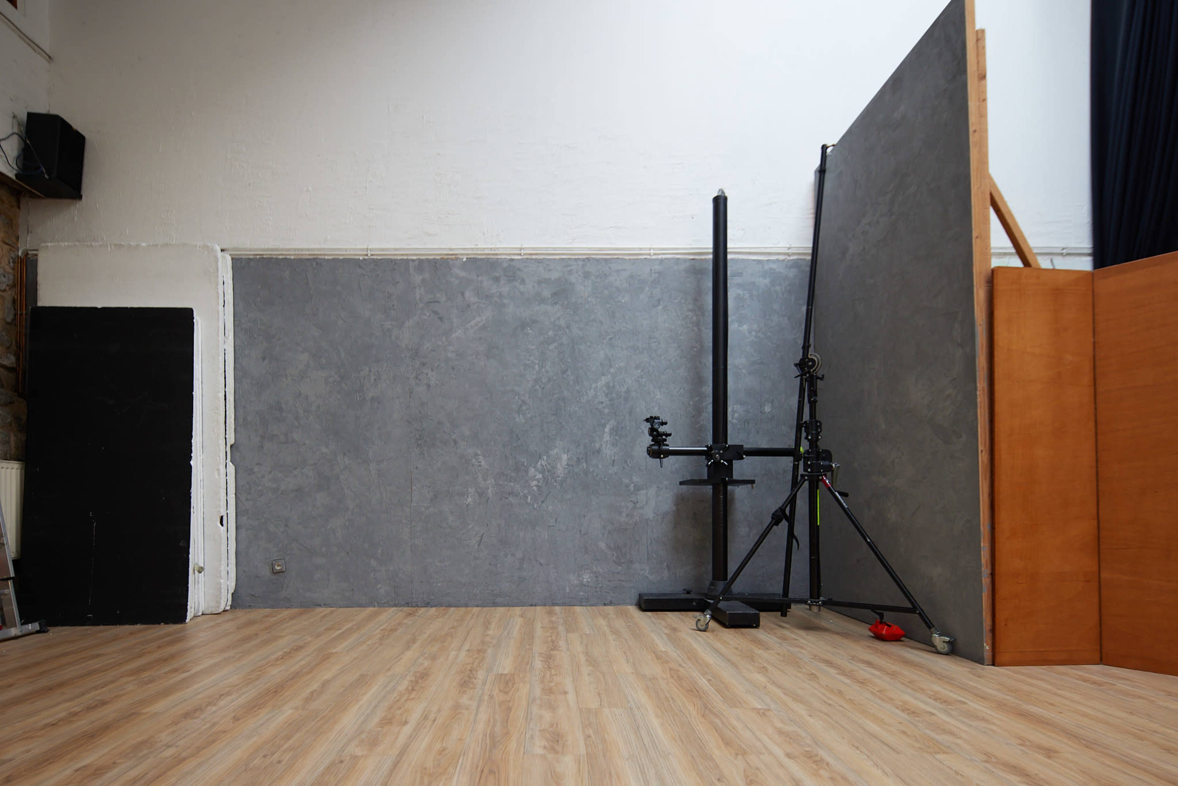 A spacious studio interior with a wooden floor and a gray backdrop supported by a tripod.