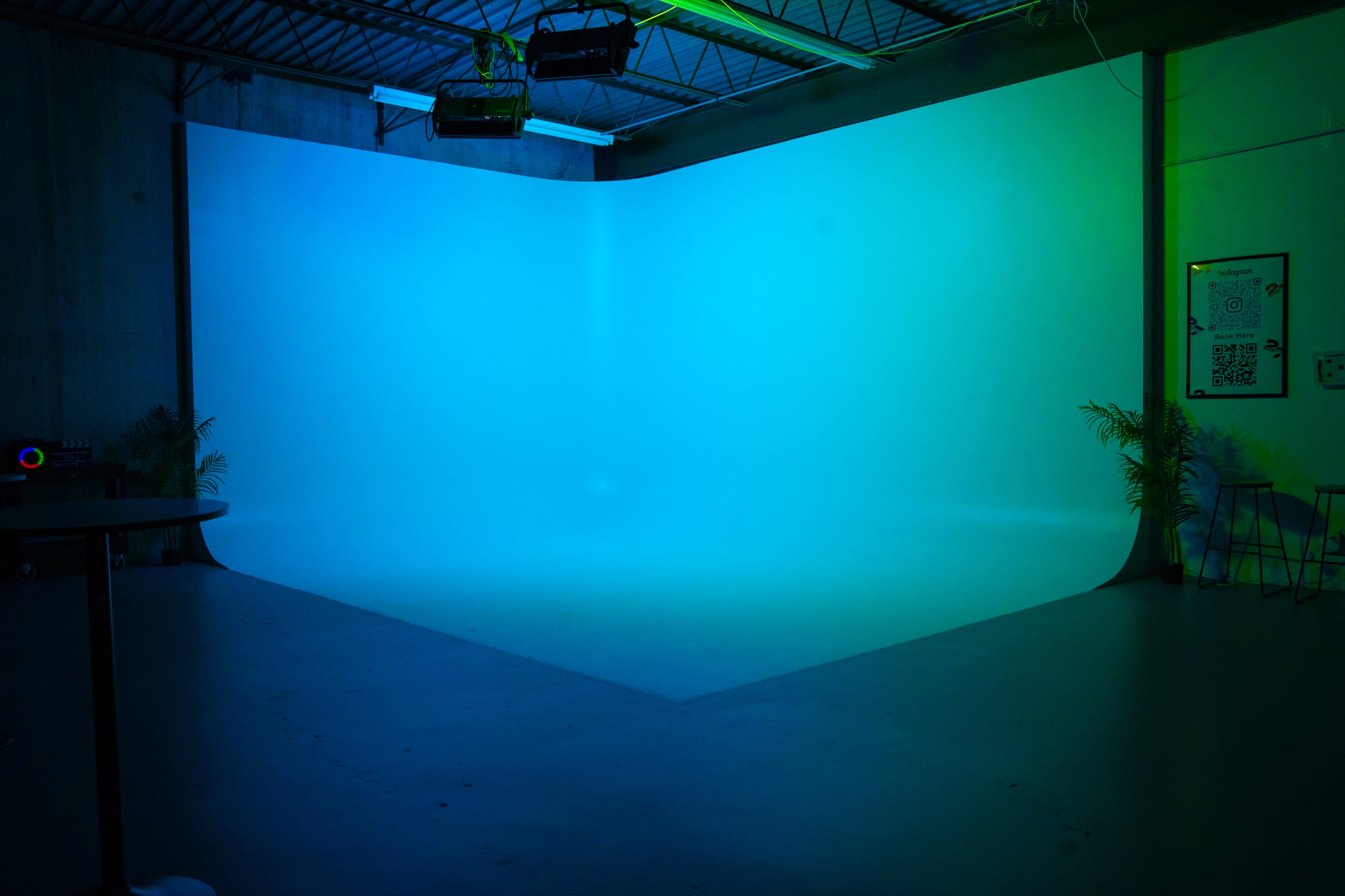 The image shows a photography studio with a smooth, curved backdrop illuminated in shades of blue and green.