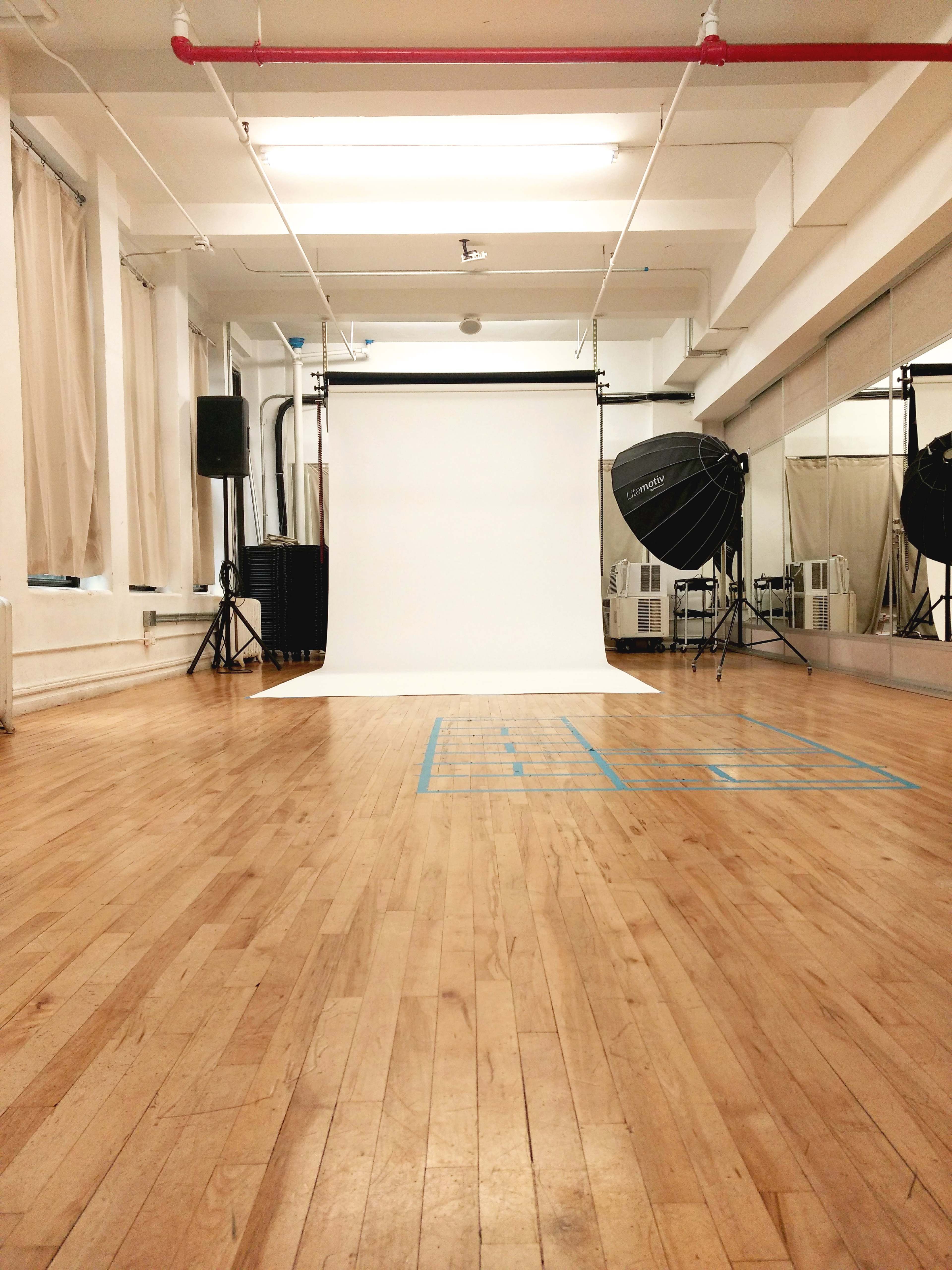 A photography studio with a blank backdrop, lighting equipment, and polished wooden flooring.