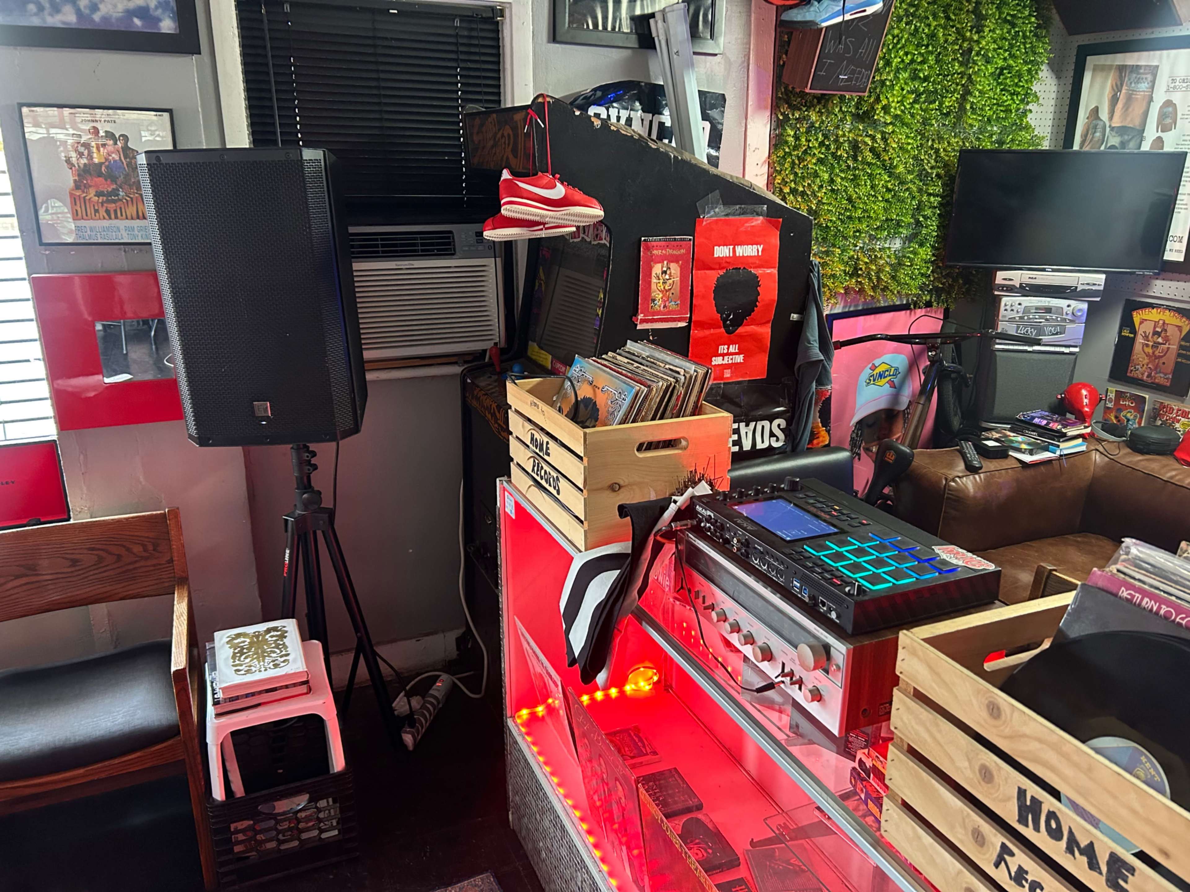 The image shows a vibrant music gathering space featuring a DJ setup with records, speakers, and a colorful display of memorabilia on the walls.