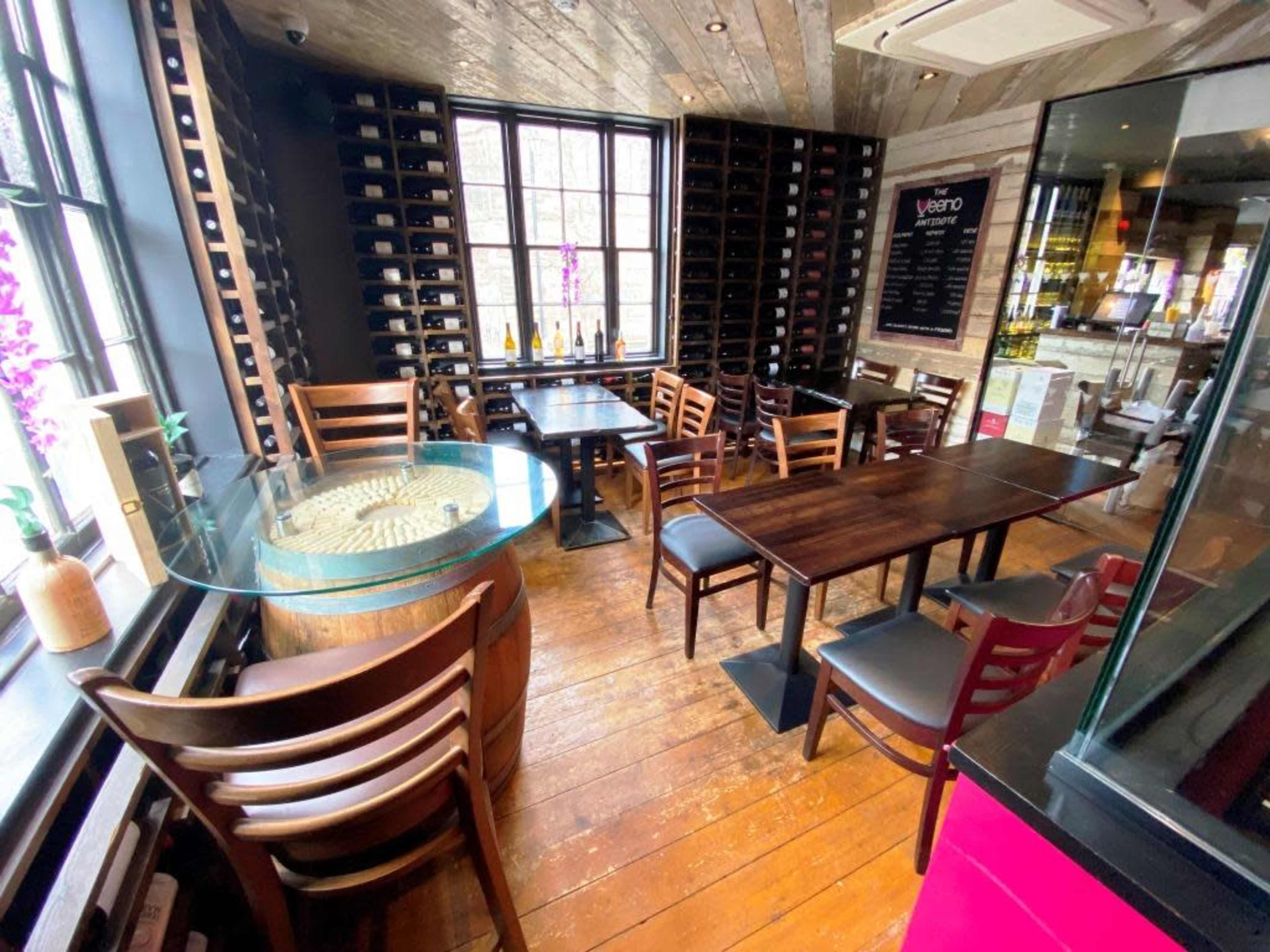 The image shows a cozy restaurant interior with wooden flooring, tables, and a wall lined with wine racks.