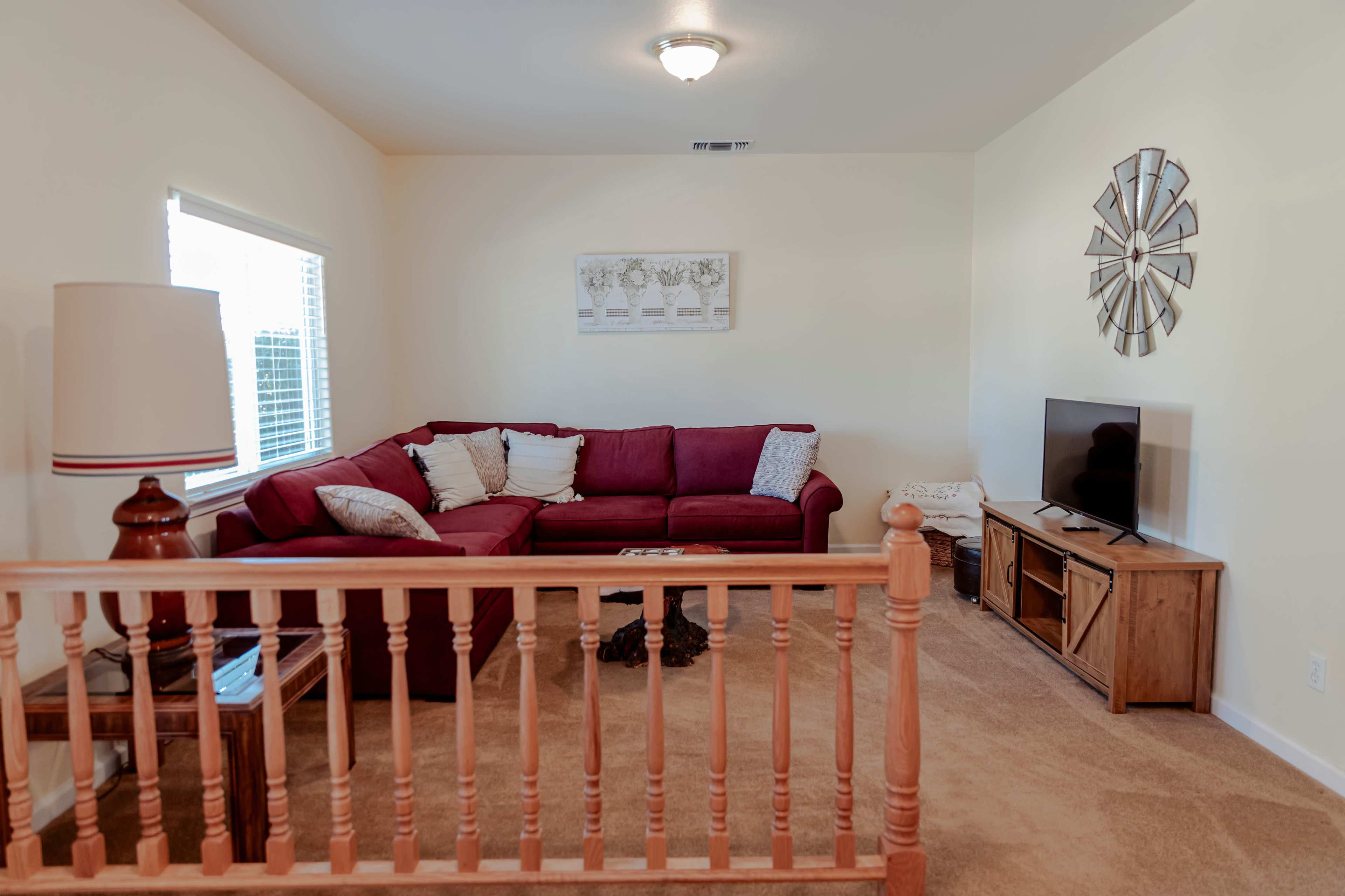 A living room features a red sectional sofa, a television on a wooden stand, and a wooden railing dividing the space.