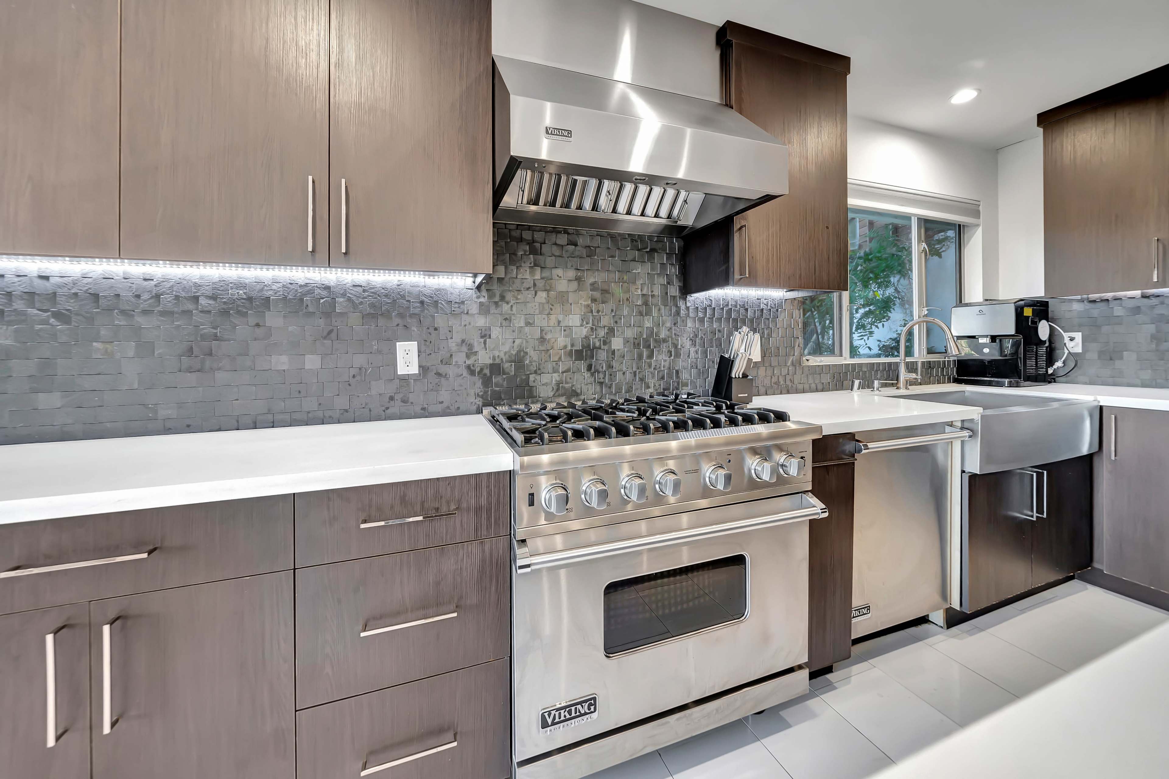 A modern kitchen features a stainless steel Viking range, a silver dishwasher, and dark wooden cabinetry with a tiled backsplash.