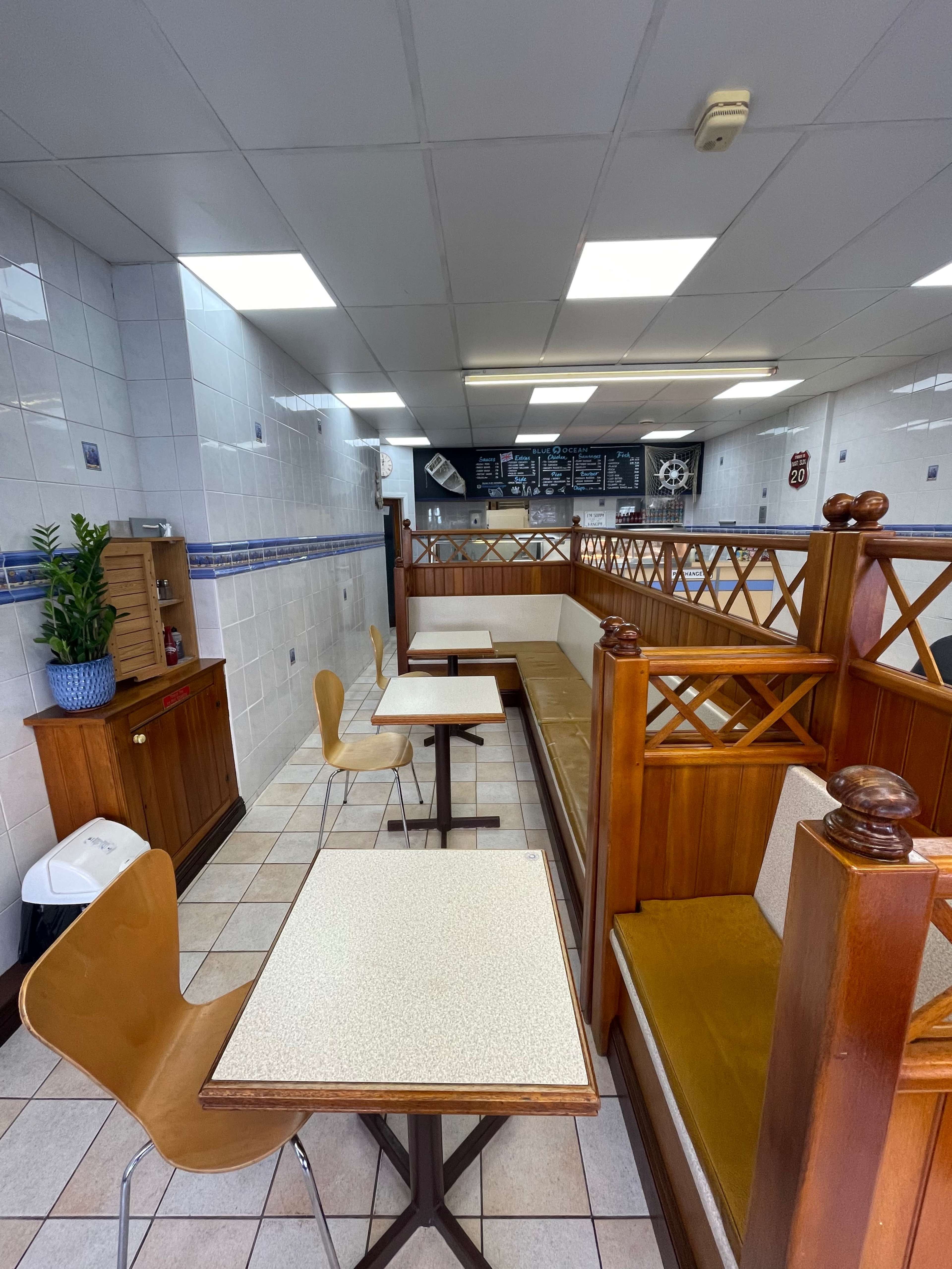 A small cafe interior with wooden seating, tables, and a counter displaying the menu in the background.