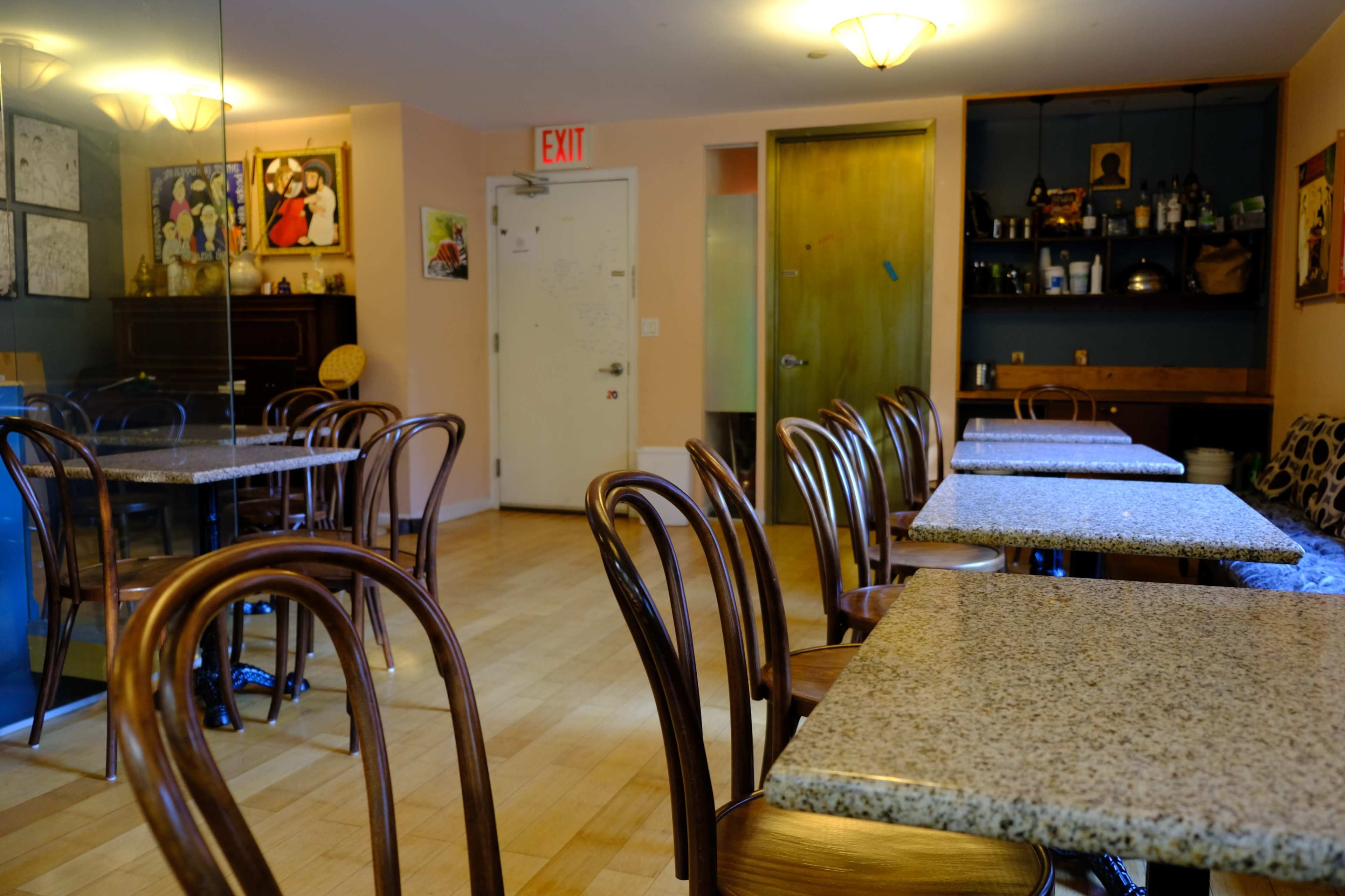 A small café interior features wooden chairs and tables with granite tops, alongside beige walls and a partially visible exit door.