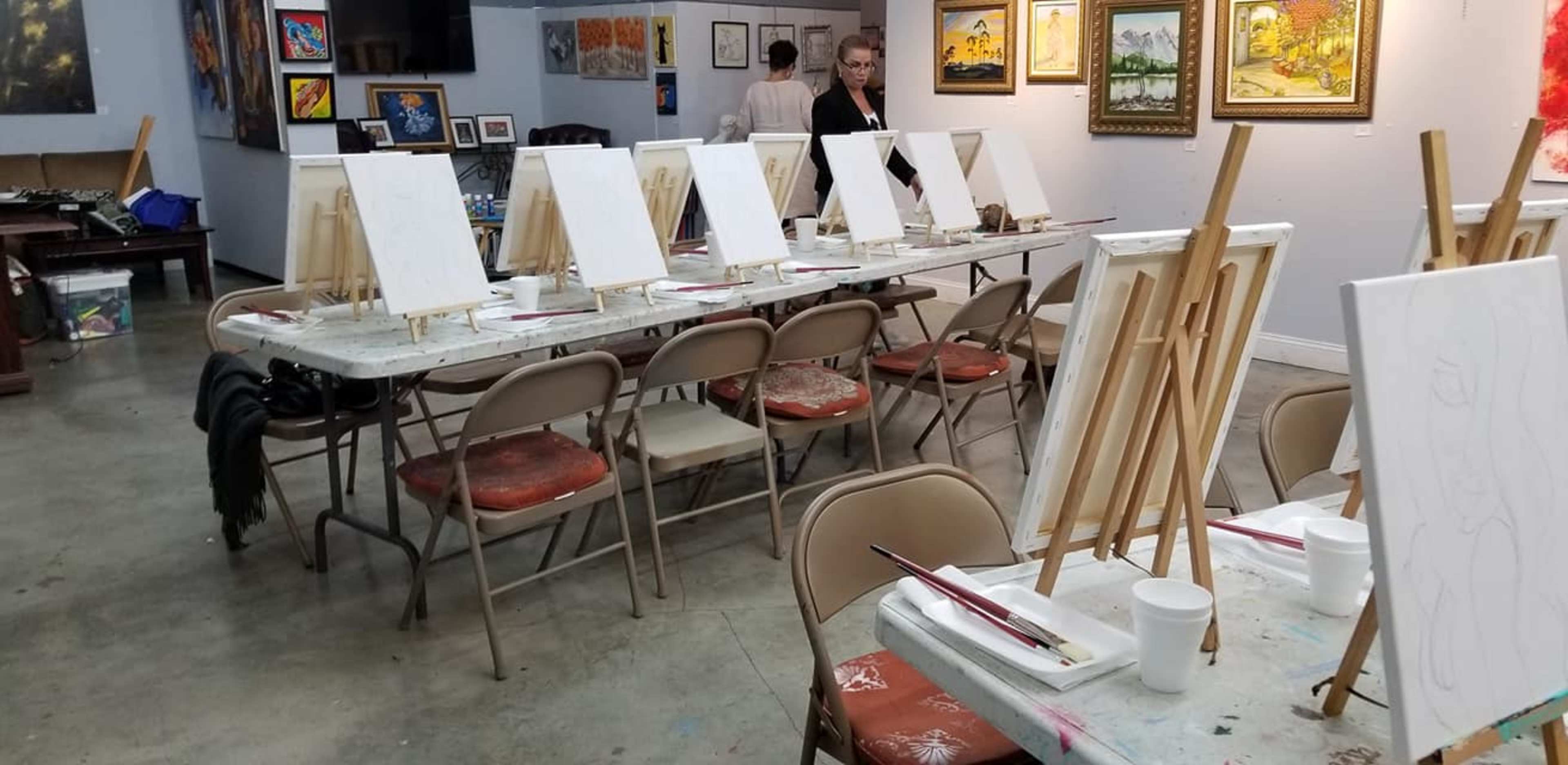 A studio setup with rows of empty canvases on easels, paintbrushes, and cups of water on tables, ready for a painting session.